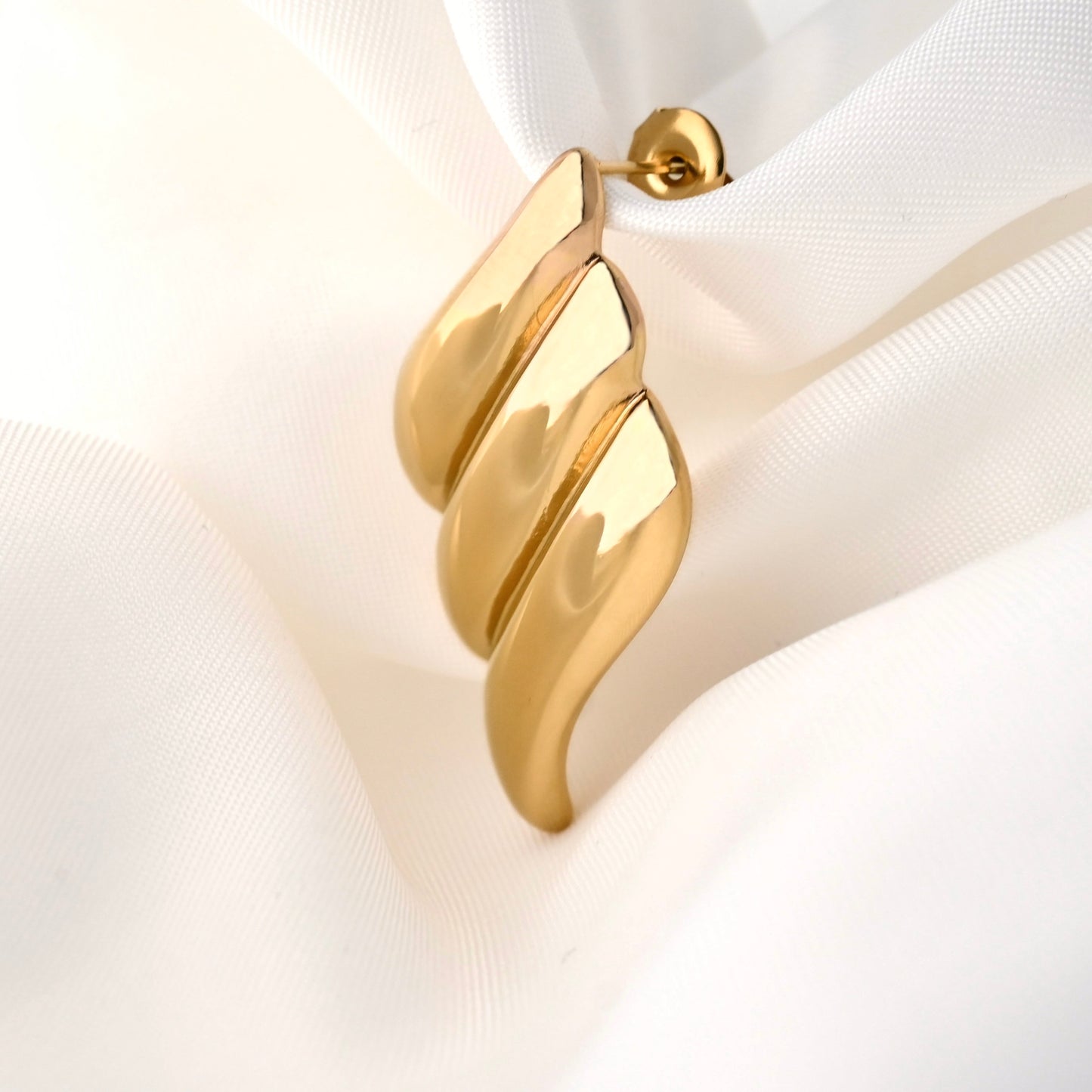 Gold diamond shaped textured drop earrings on a white fabric background
