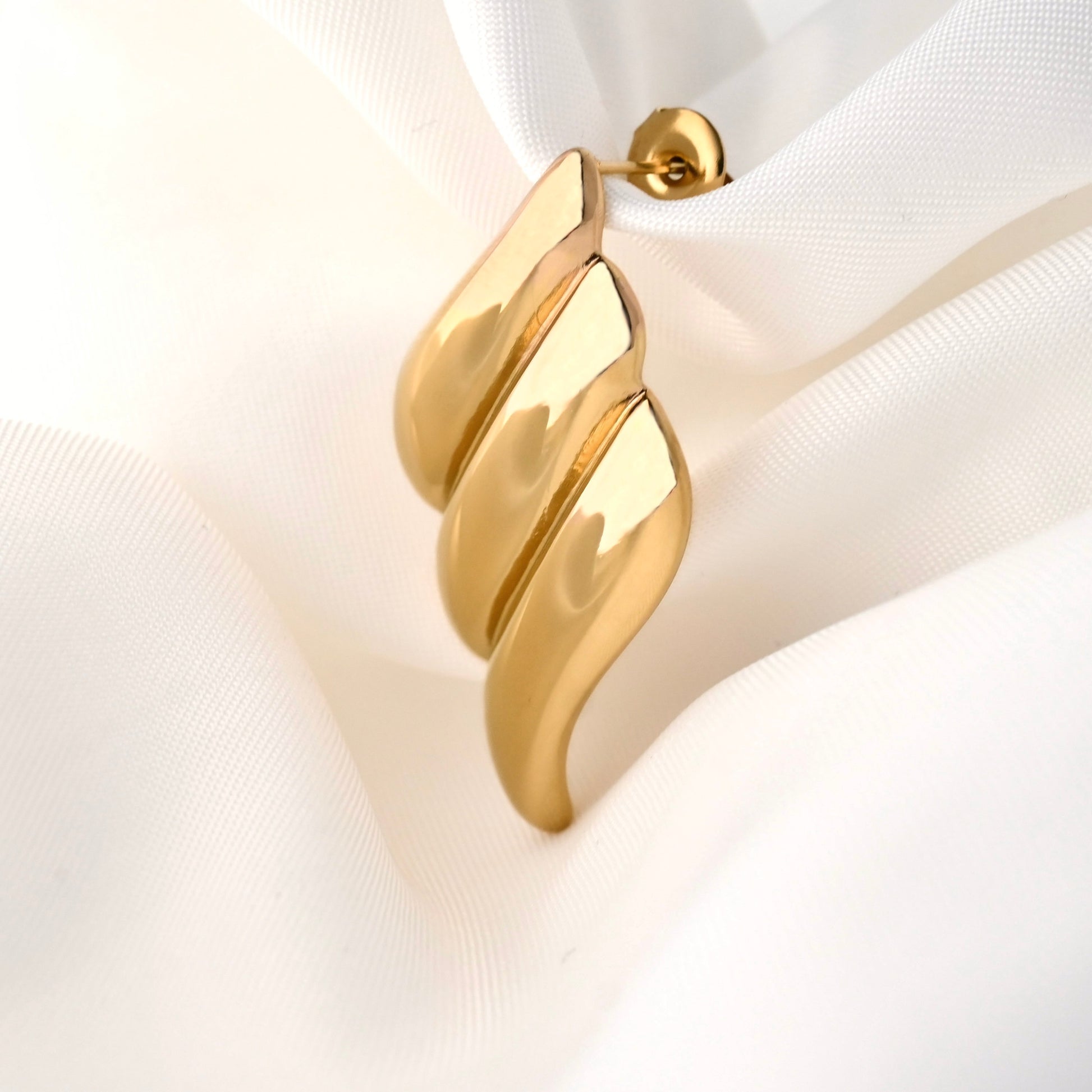 Gold diamond shaped textured drop earrings on a white fabric background