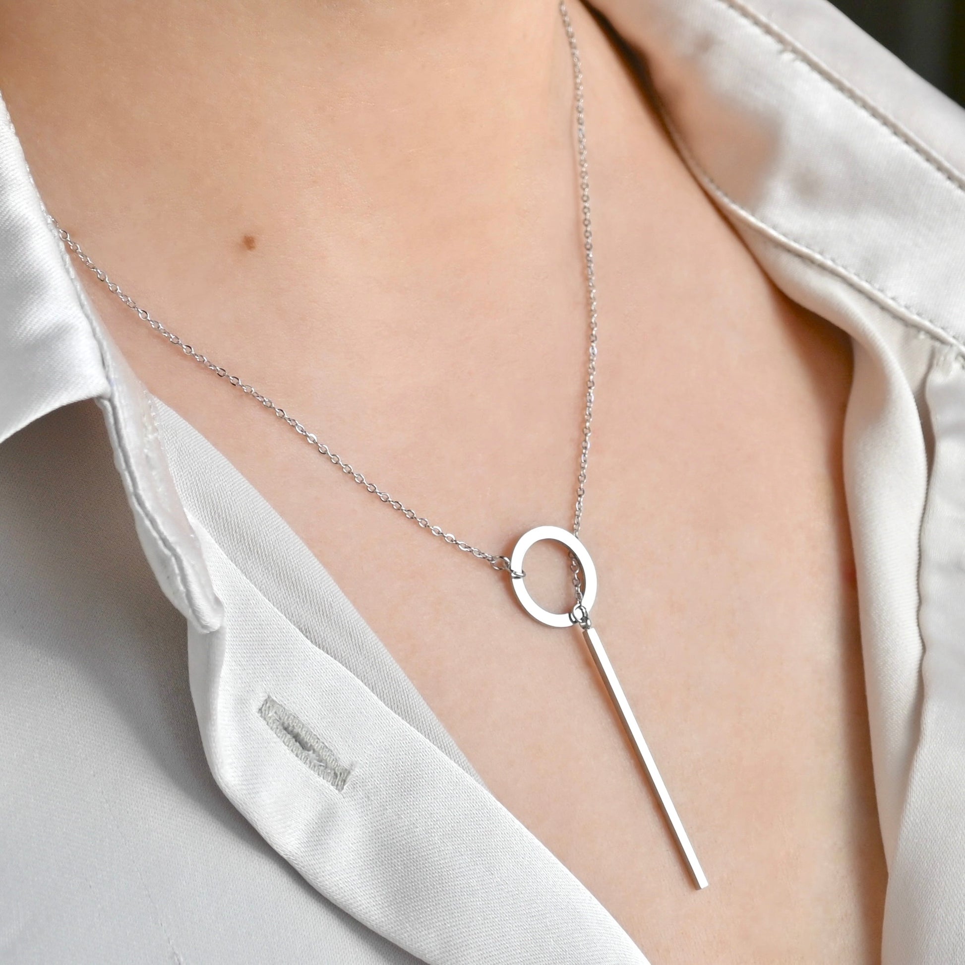 Silver geometric necklace on a person wearing a white shirt.
