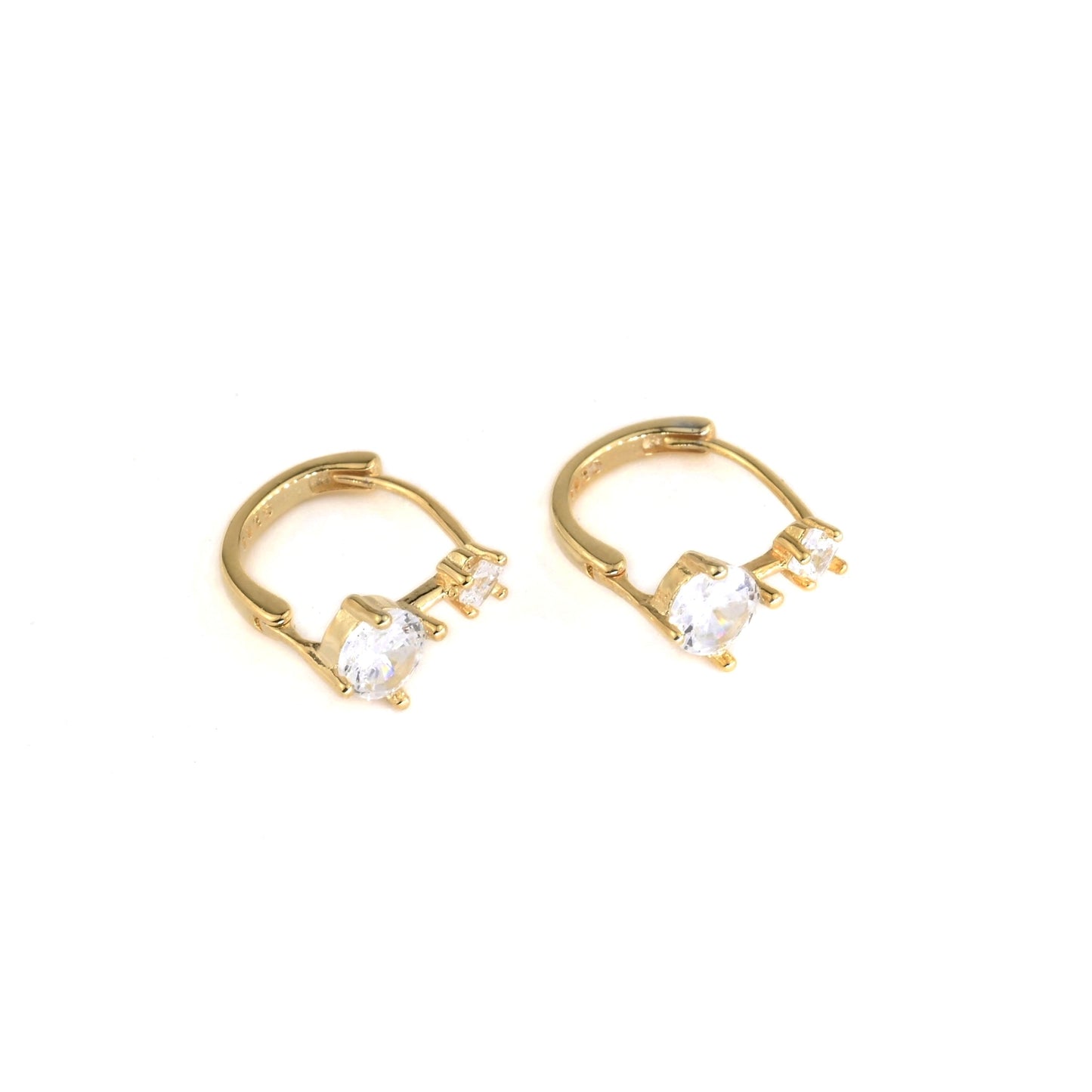 Gold huggie hoop earrings with one medium and one small clear gemstones on a white background