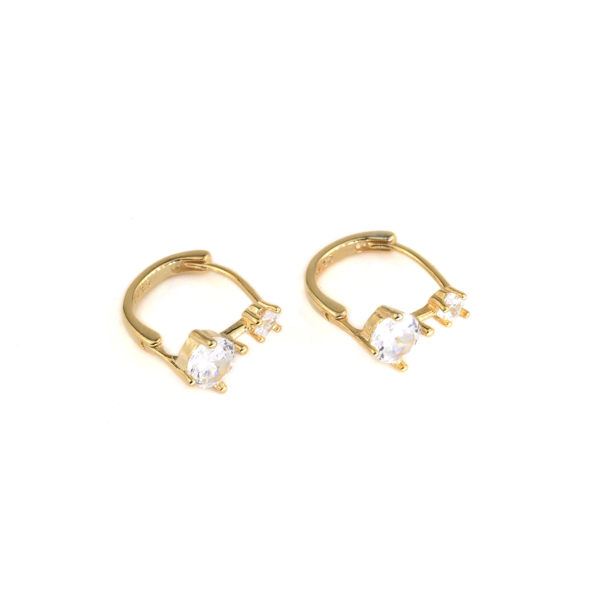Gold huggie hoop earrings with one medium and one small clear gemstones on a white background