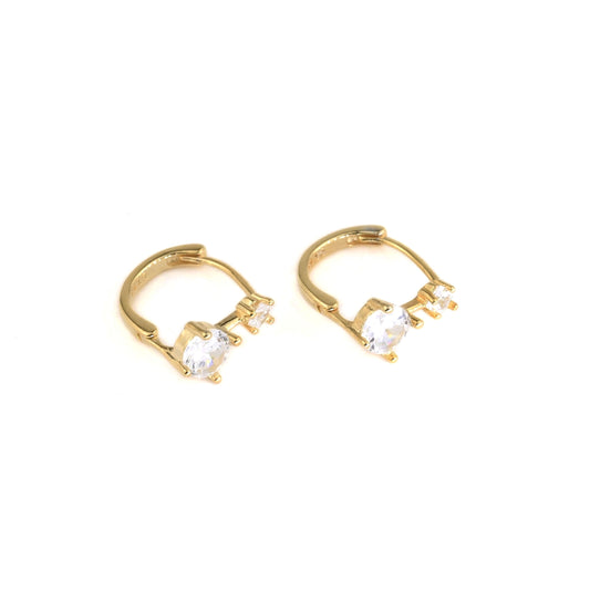 Gold huggie hoop earrings with one medium and one small clear gemstones on a white background