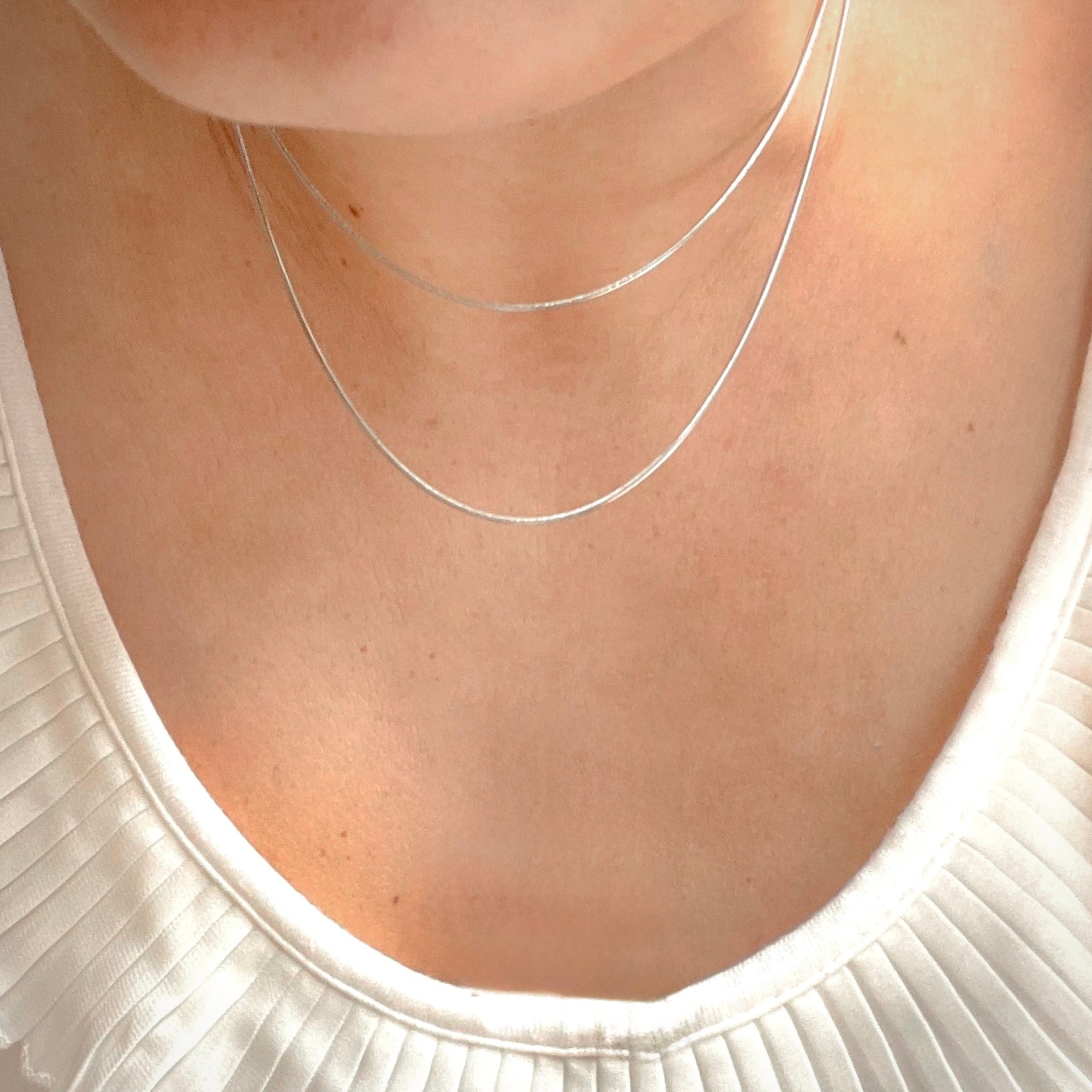 Close-up of a person wearing a thin silver necklace against a neutral background