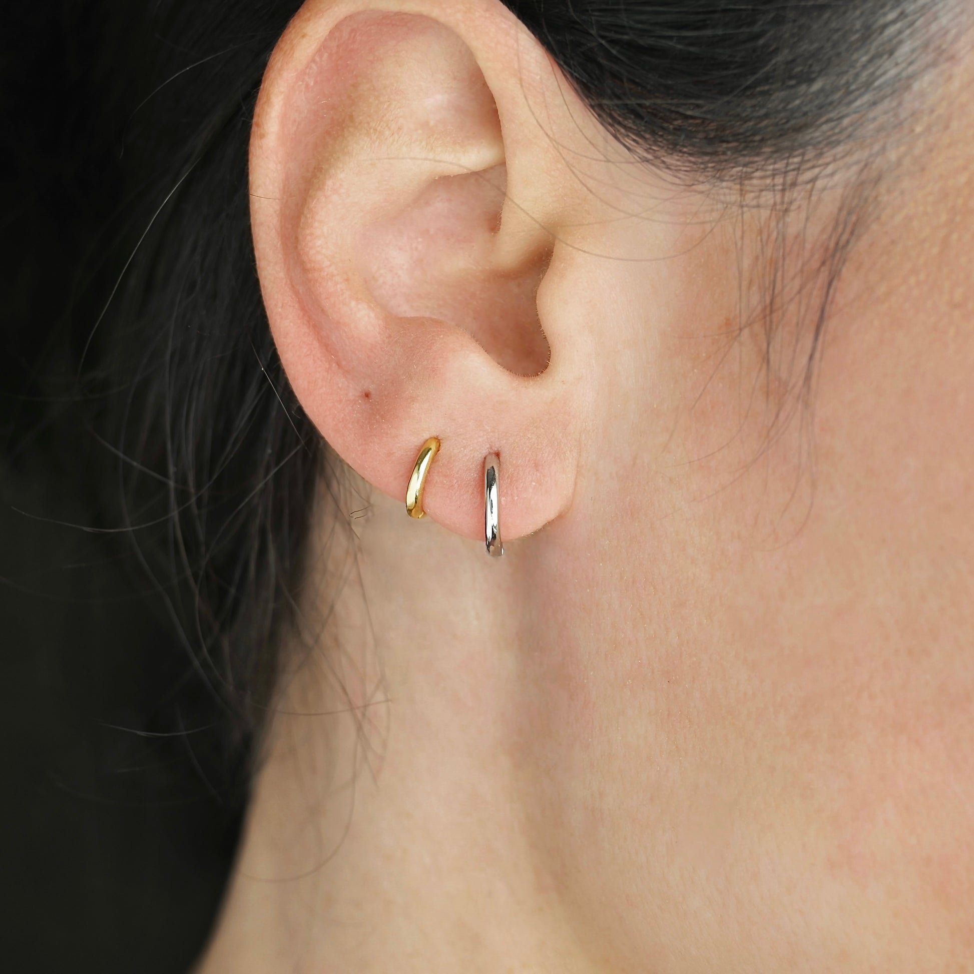 Close-up of an ear wearing gold and silver hoop earrings with a blurred background.