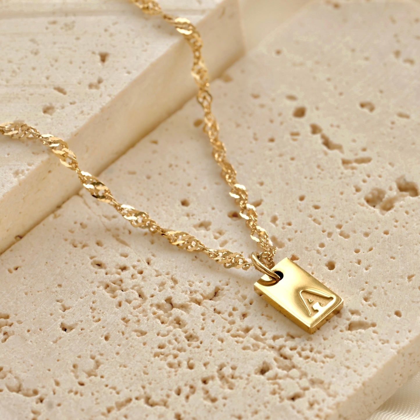 Gold singapore chain necklace with an initial pendant on a textured beige surface
