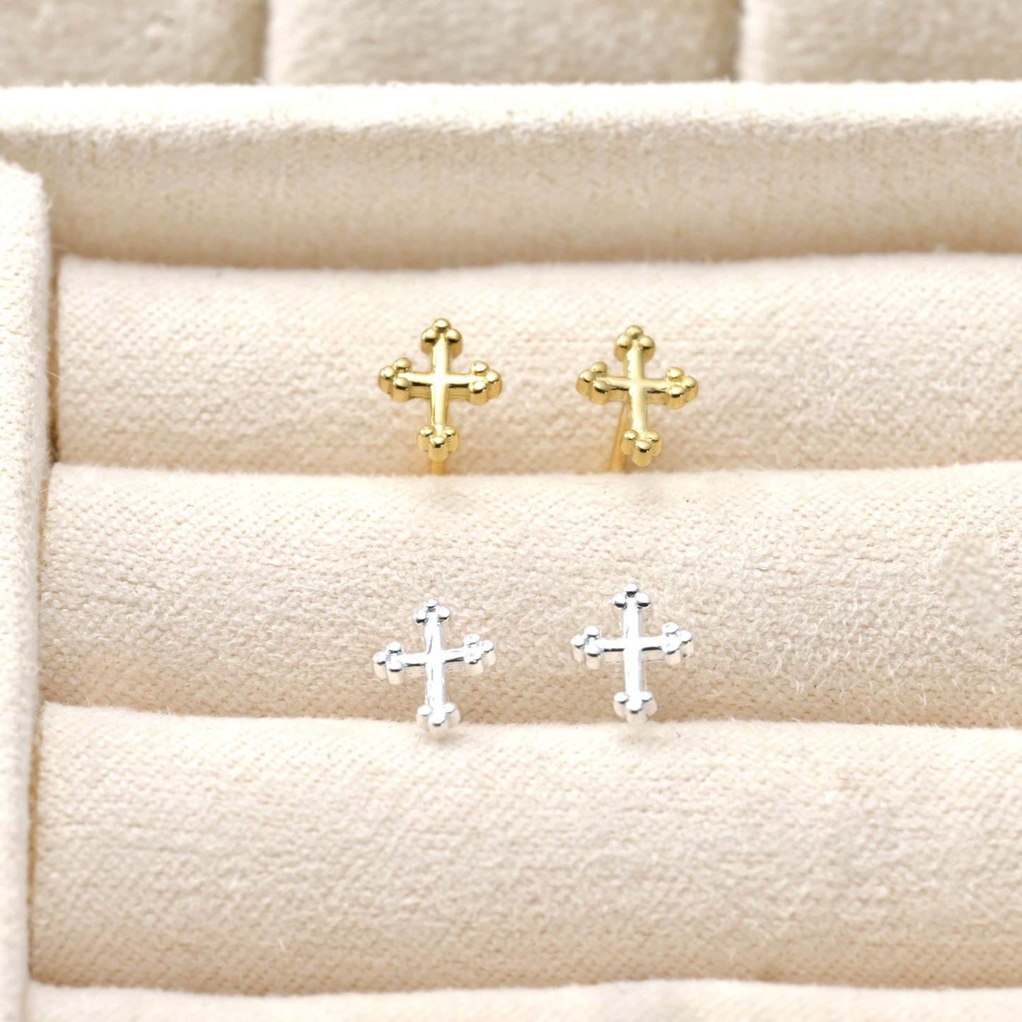 A pairof Gold and silver cross earrings on a textured beige surface