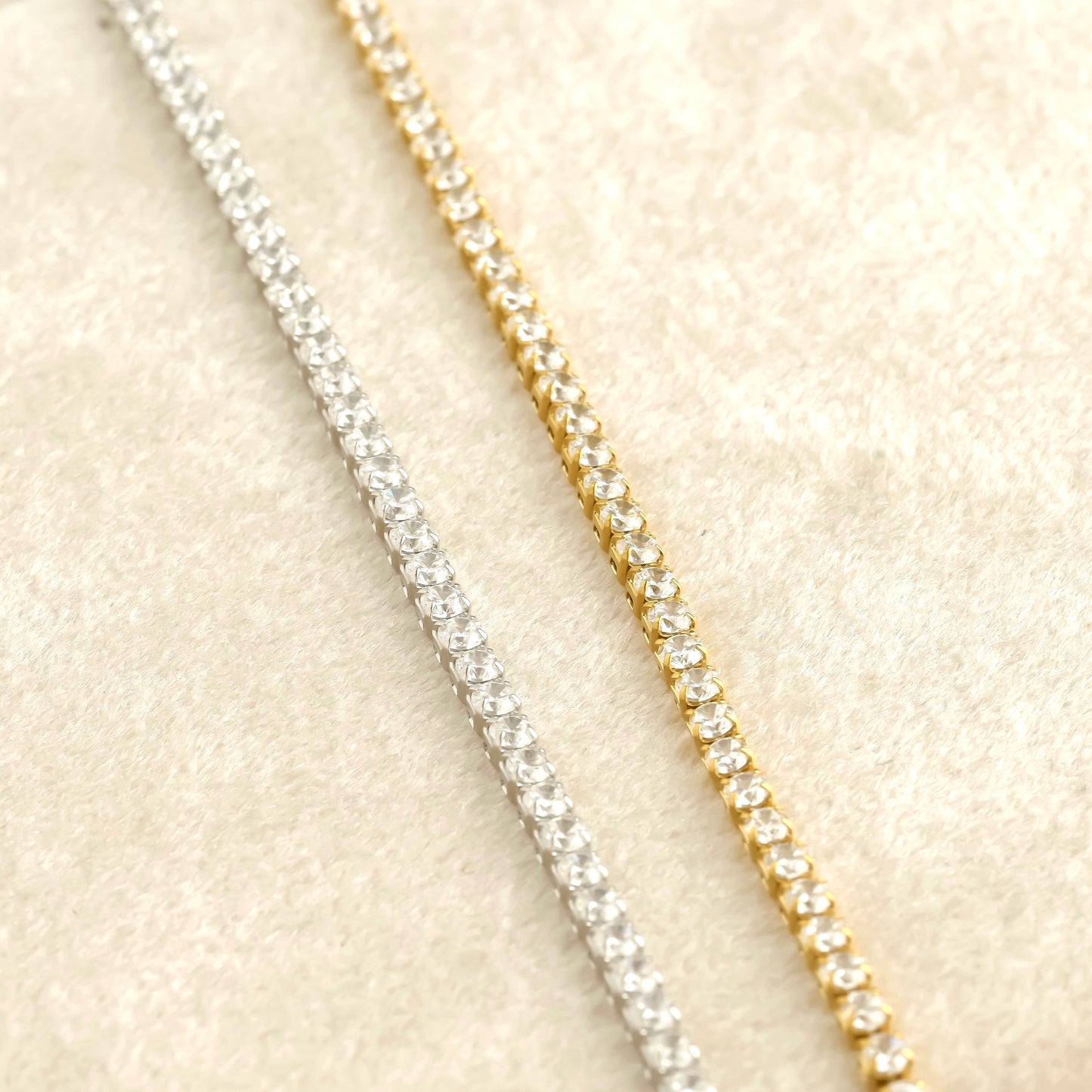 Two diamond chains, one silver and one gold, on a beige fabric background.