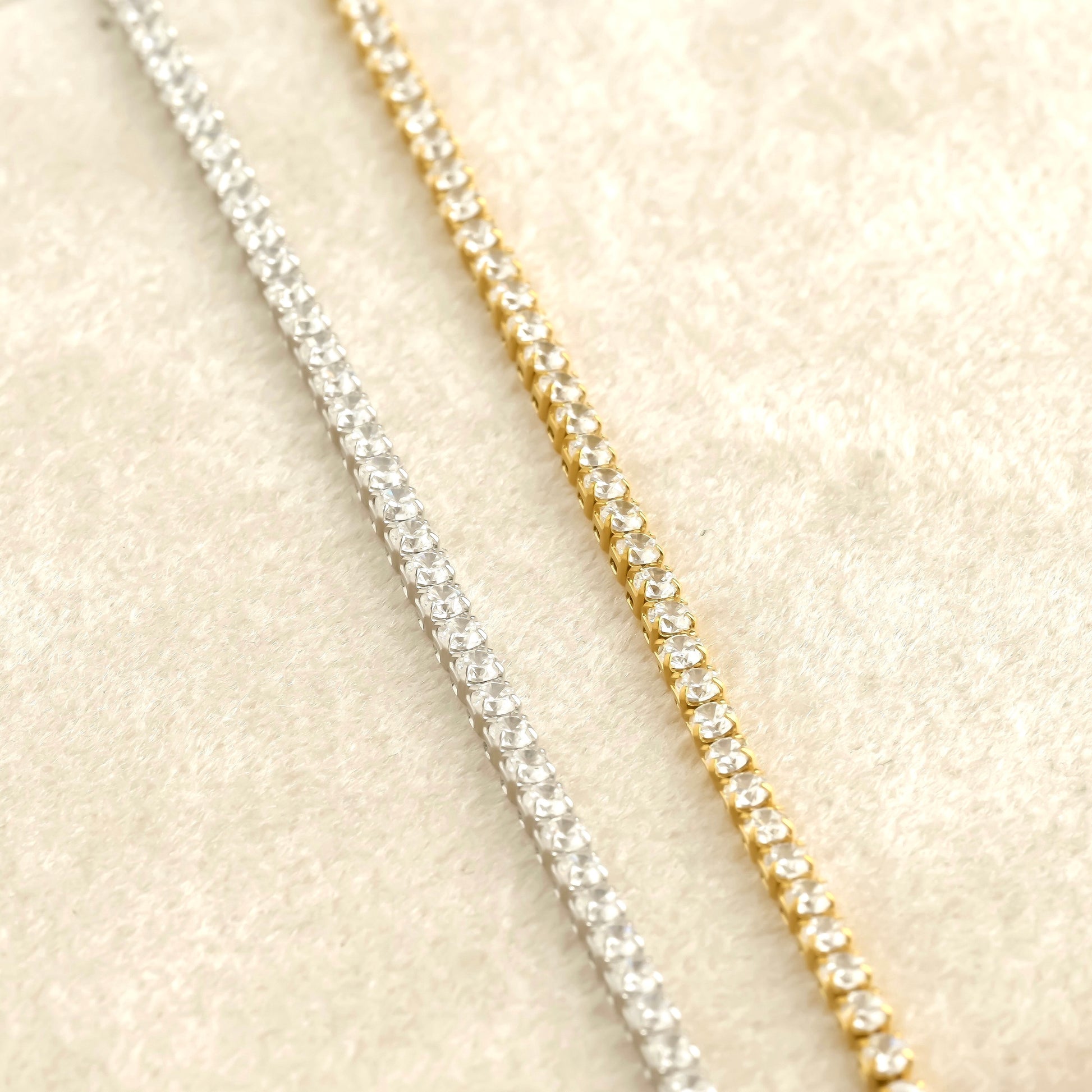 Two diamond chains, one silver and one gold, on a beige fabric background.