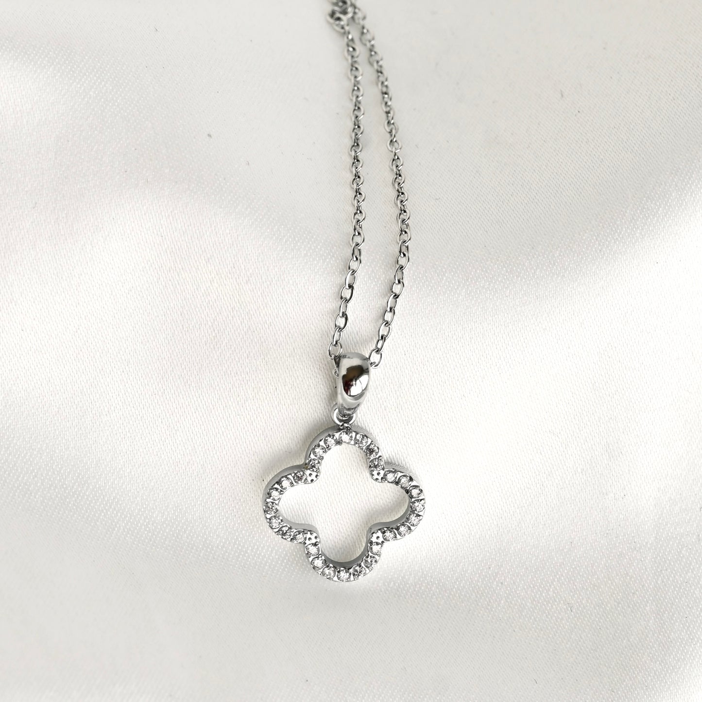 A silver-toned necklace with a four-leaf clover pendant, photographed on a white satin fabric background.