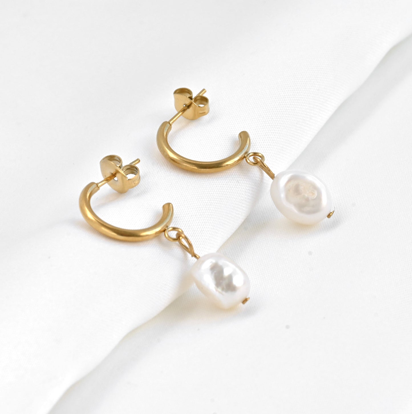 Gold C hoop earrings with freshwater pearl drops on a white background