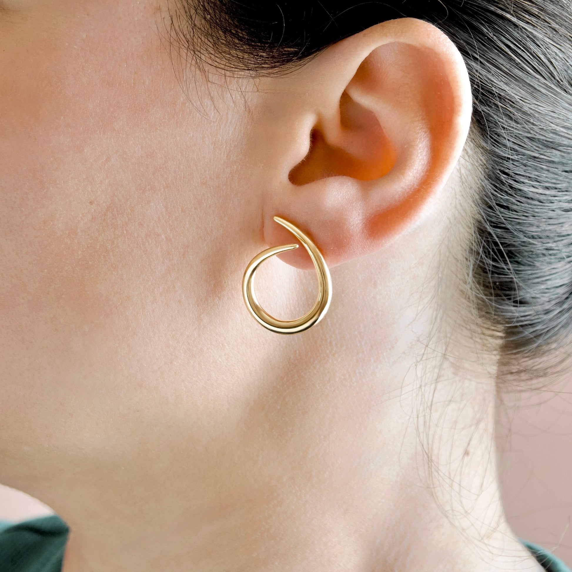 a close-up side profile view of a model wearing gold swirl hoop studs.