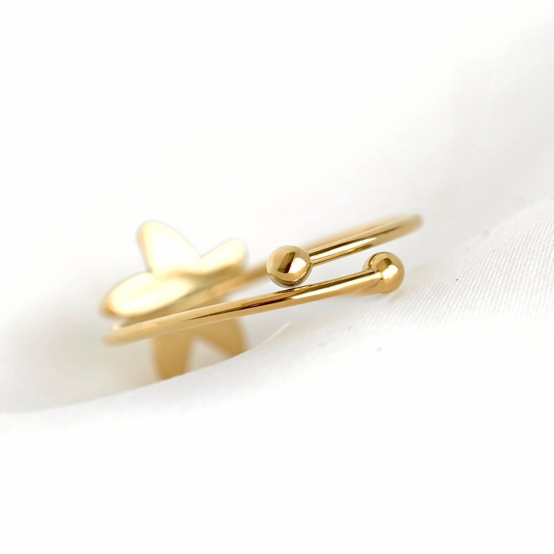A delicate gold-plated adjustable ring featuring a small sea star charm and  two ball ends, resting on a soft white textured fabric.