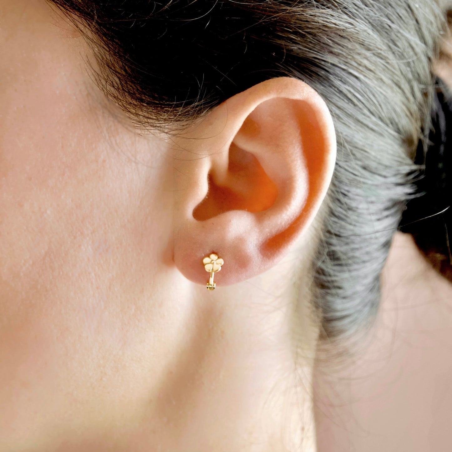 A close-up of a person's ear wearing a small gold flower-shaped stud earring.
