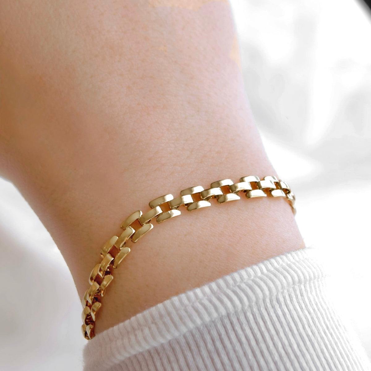 A close-up of a gold chain link bracelet worn on a person's wrist, paired with a white ribbed knit sleeve.