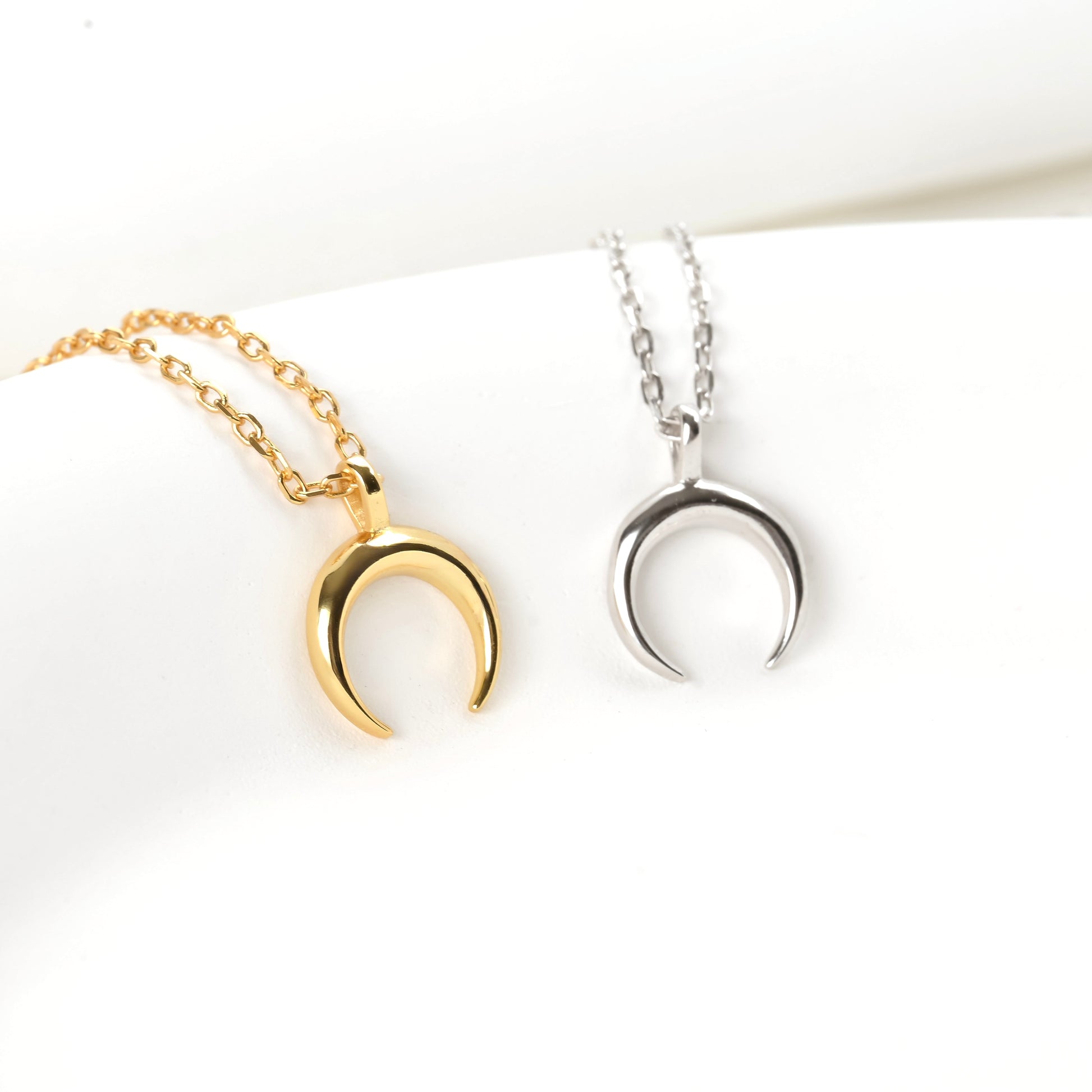 Two crescent pendants, one gold and one silver, on white backgrounds.
