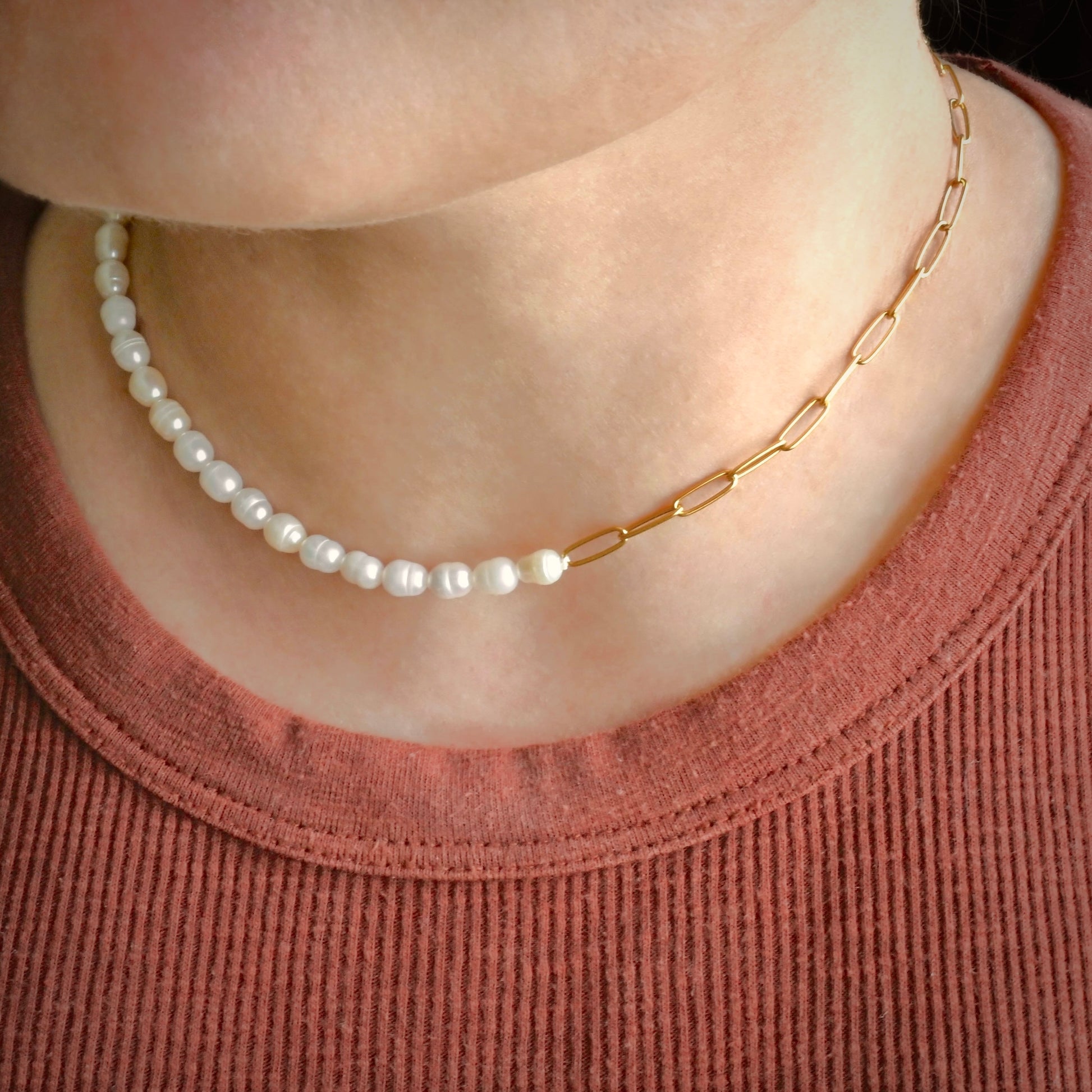 Pearl necklace and gold chain on a person wearing a pink shirt