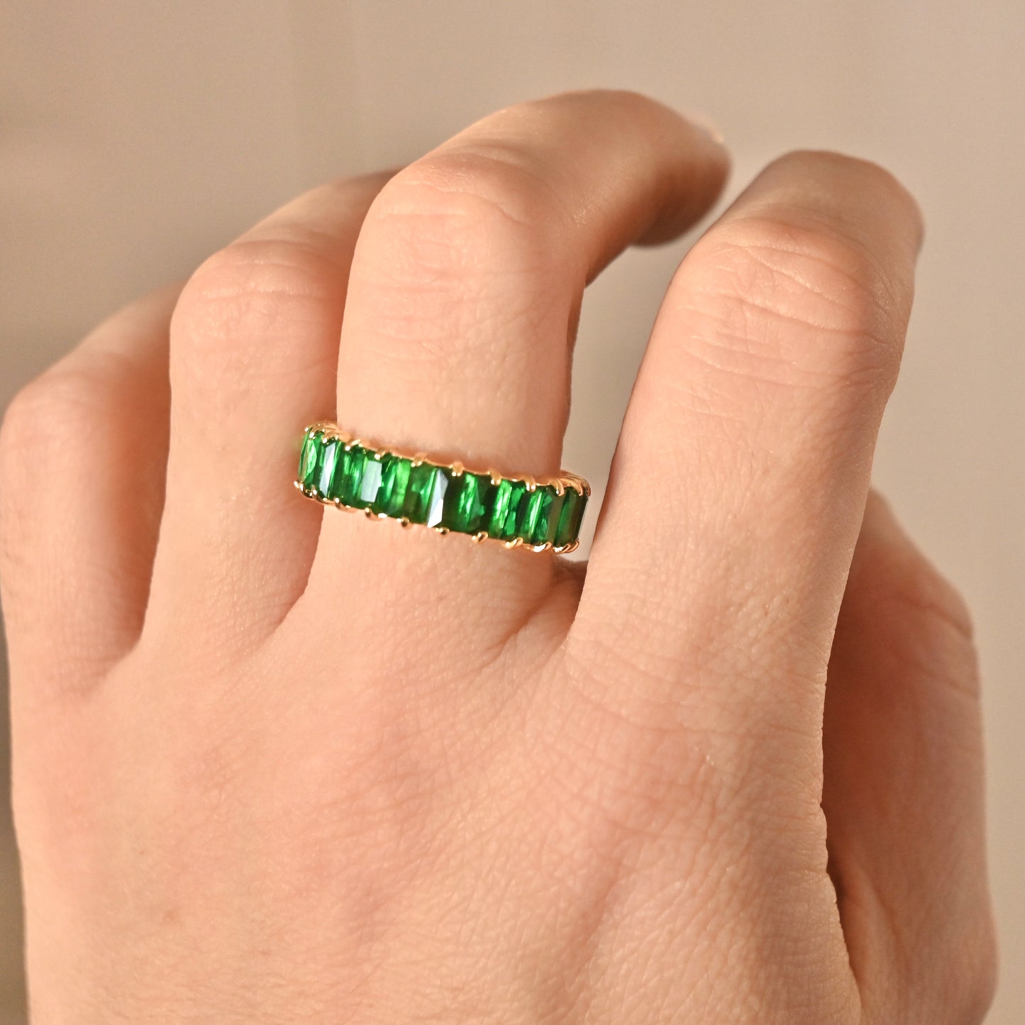 may birthstone ring on a person's finger against a beige background
