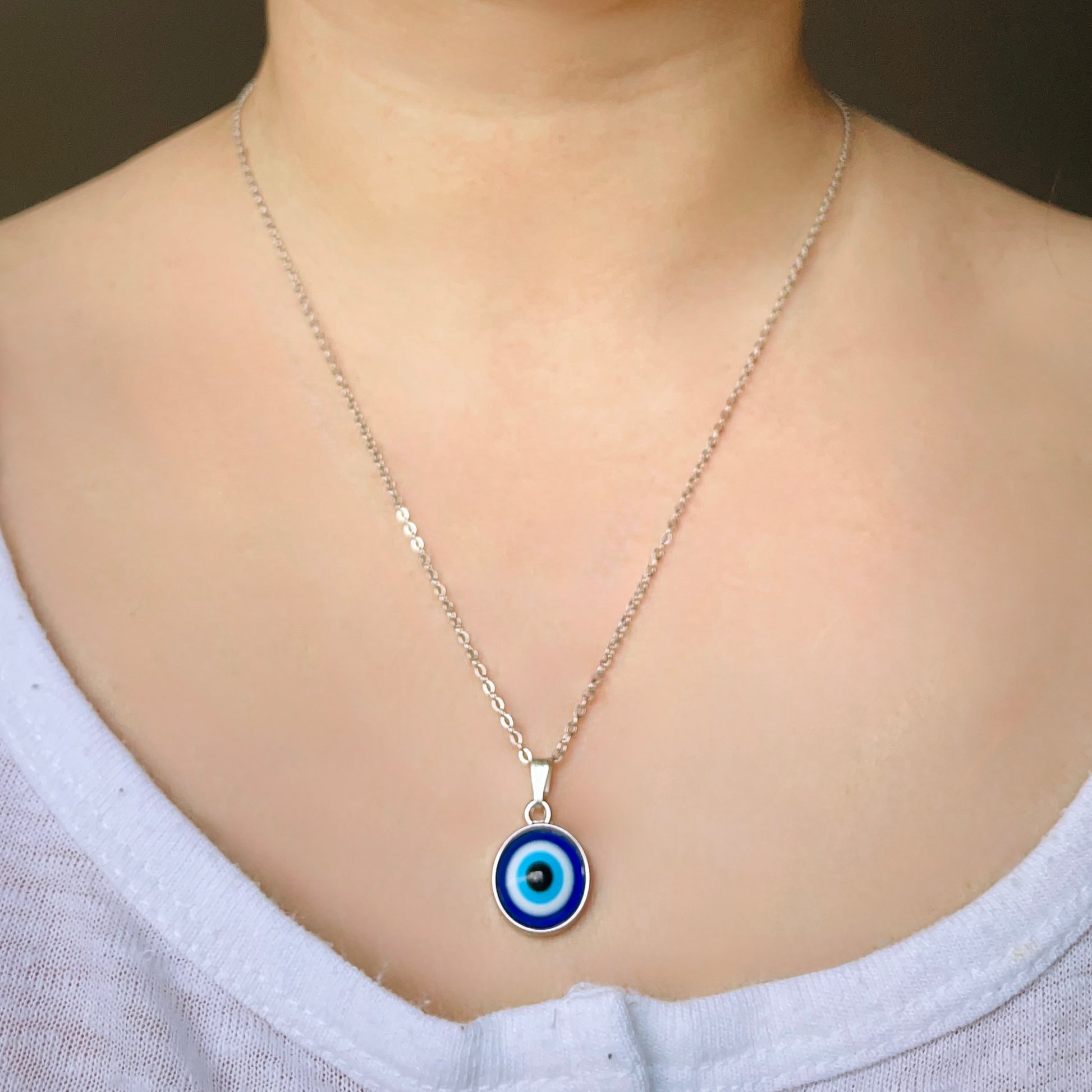 Front view of woman wearing a silver chain necklace with a blue evil eye pendant 