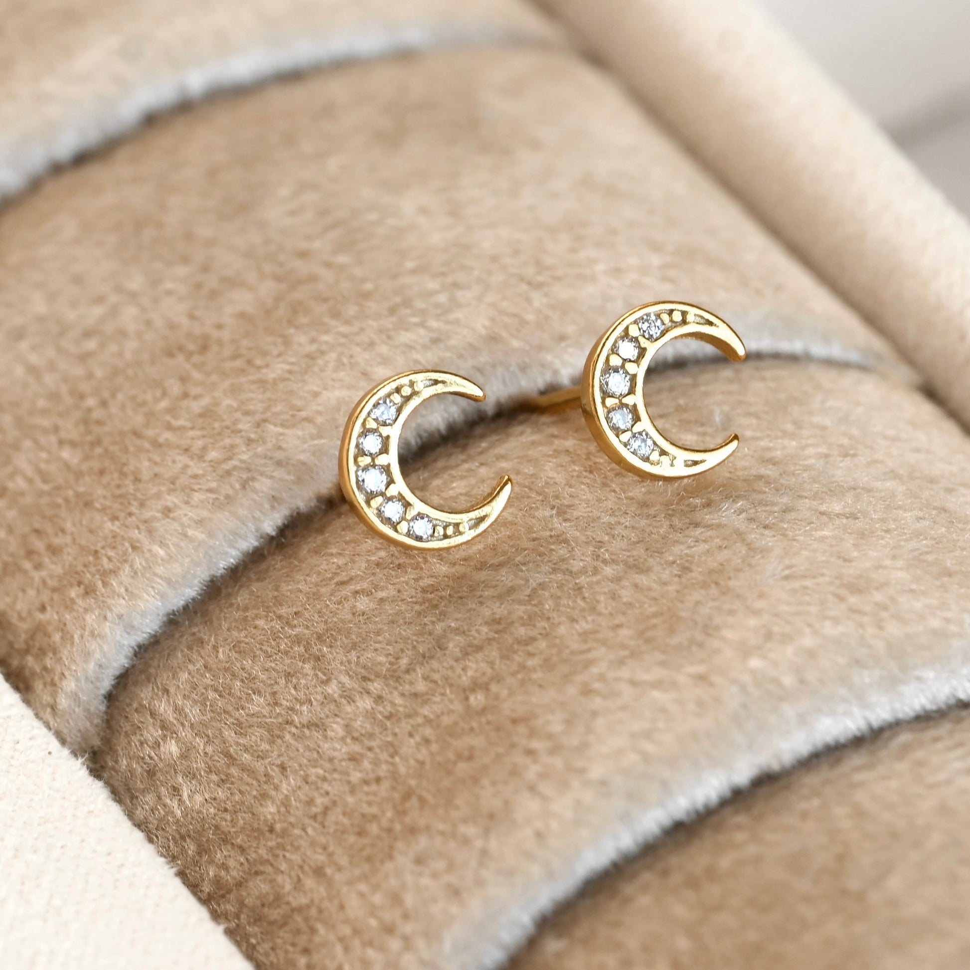 Gold moon earrings with pave CZ stones on a soft fabric background