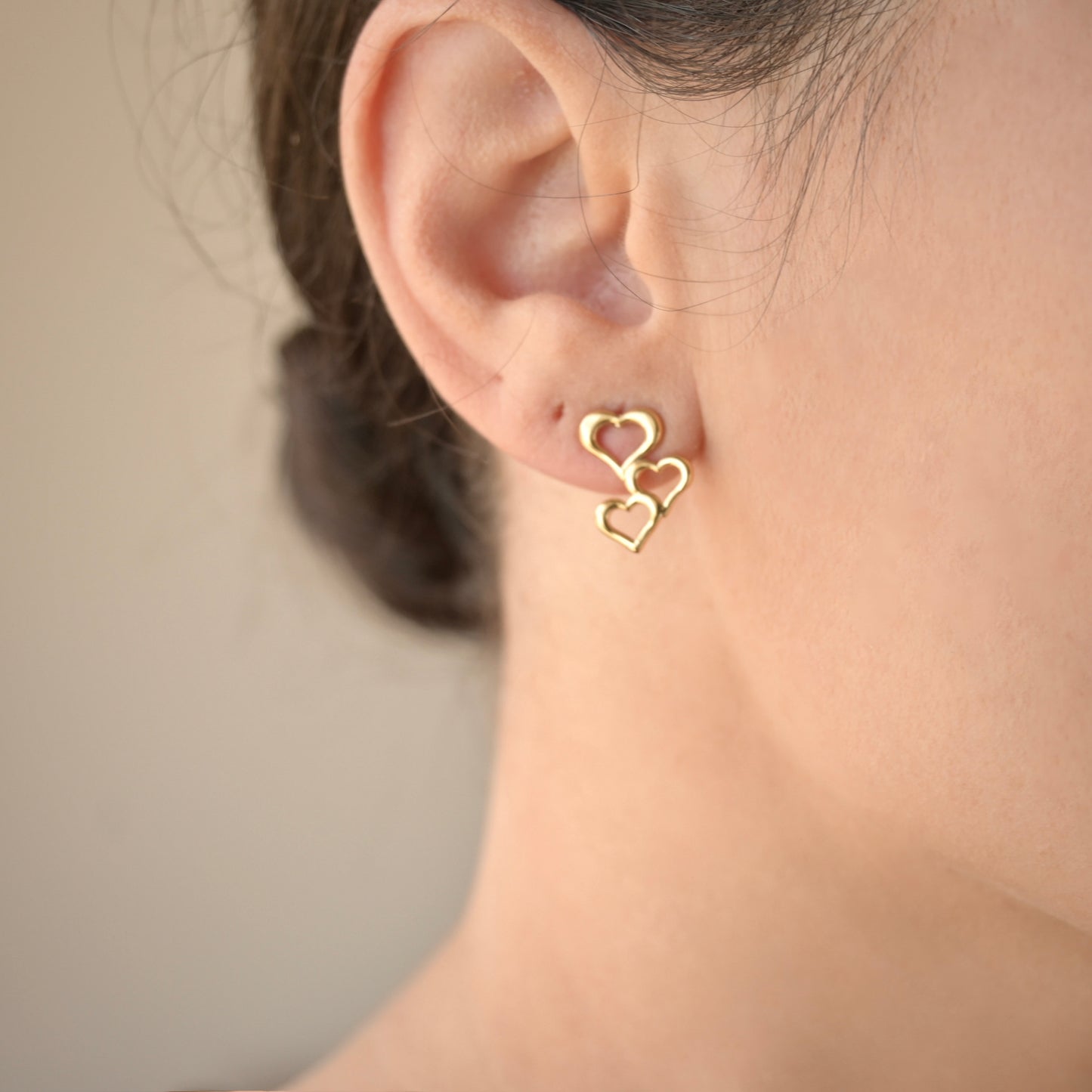 Gold heart earrings worn by a person with a neutral background