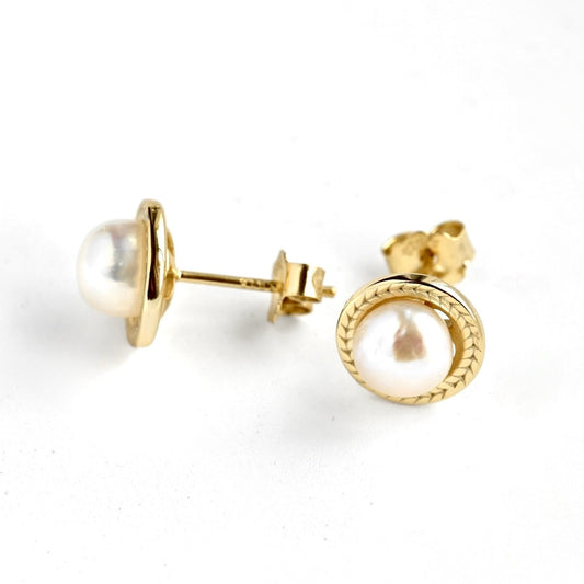 A pair of gold stud earrings with round white freshwater pearls, one shown from the front and the other from the side/back.