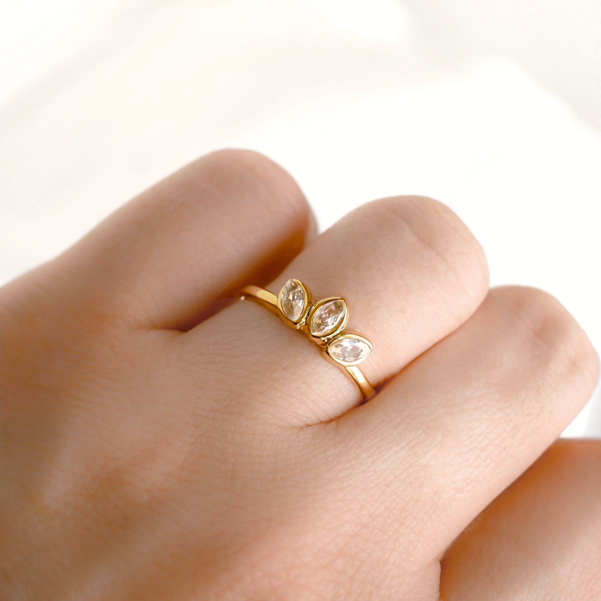 A close-up of a hand wearing a delicate gold lotus ring with three marquise-cut clear stones set in a row.