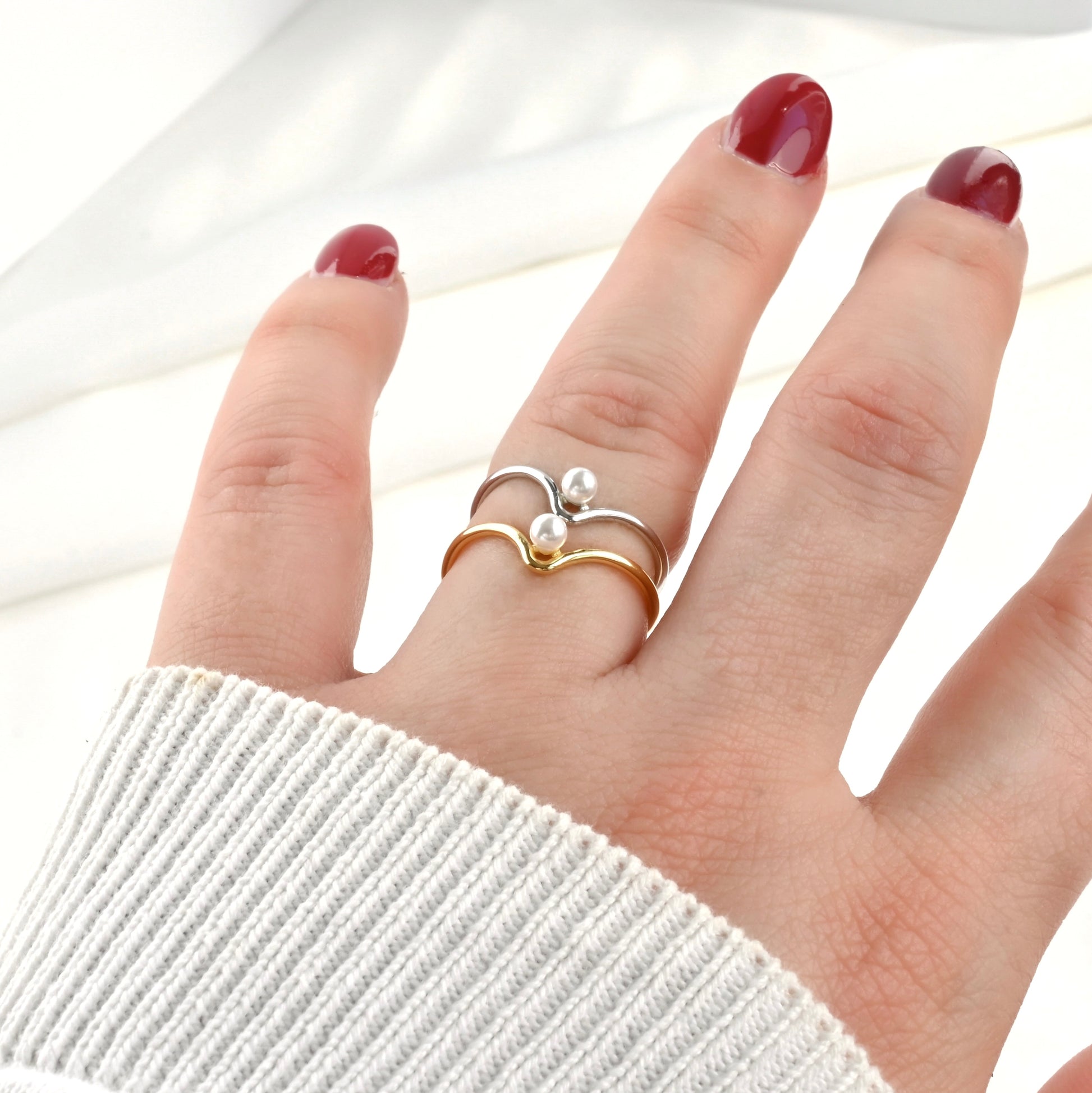 Hand wearing a gold and silver open pearl rings stacked on the same finger on a white background