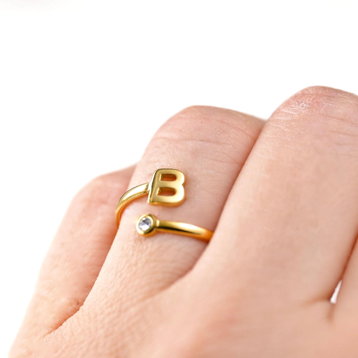 Gold ring with letter 'B' on a finger against a white background