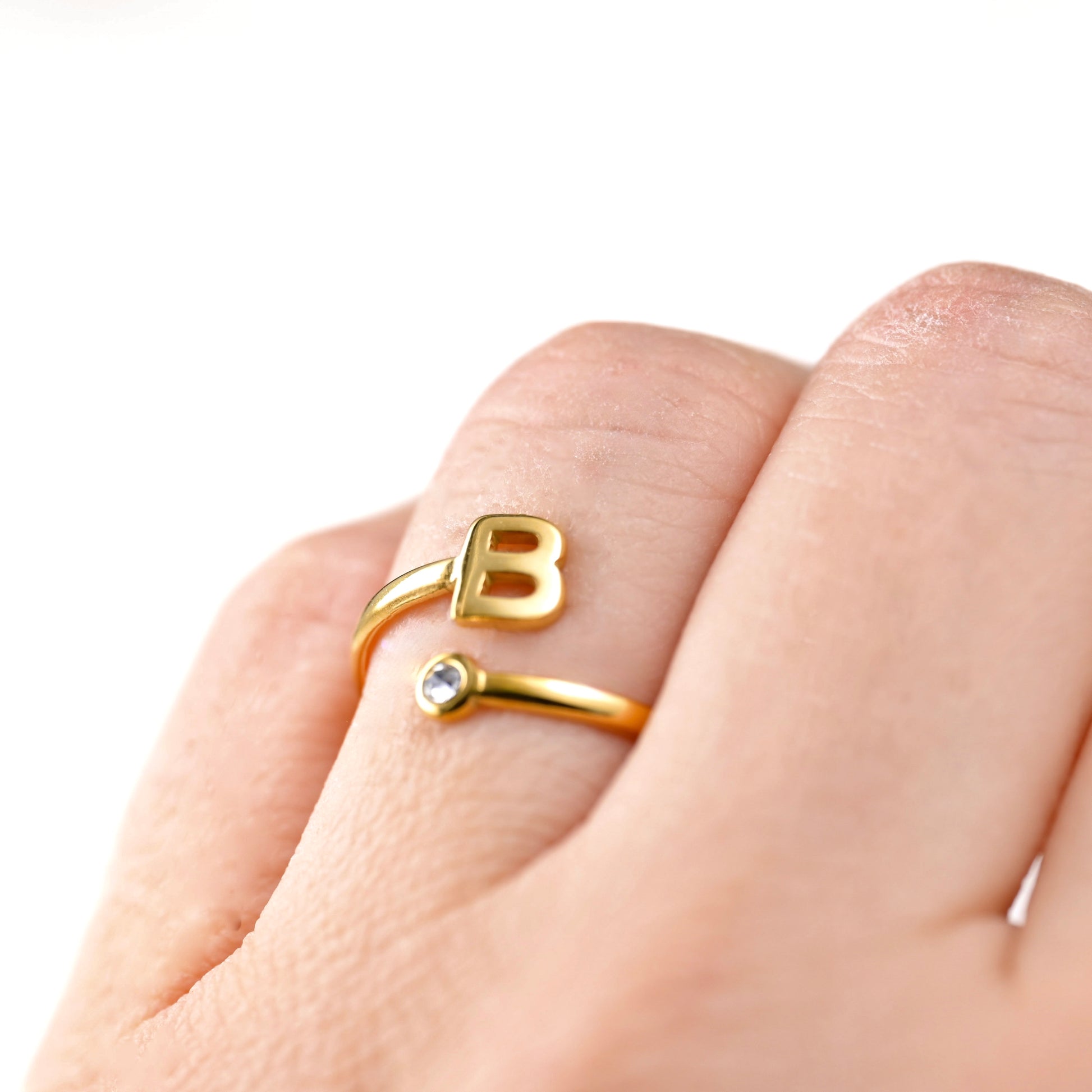 Gold ring with letter 'B' on a finger against a white background