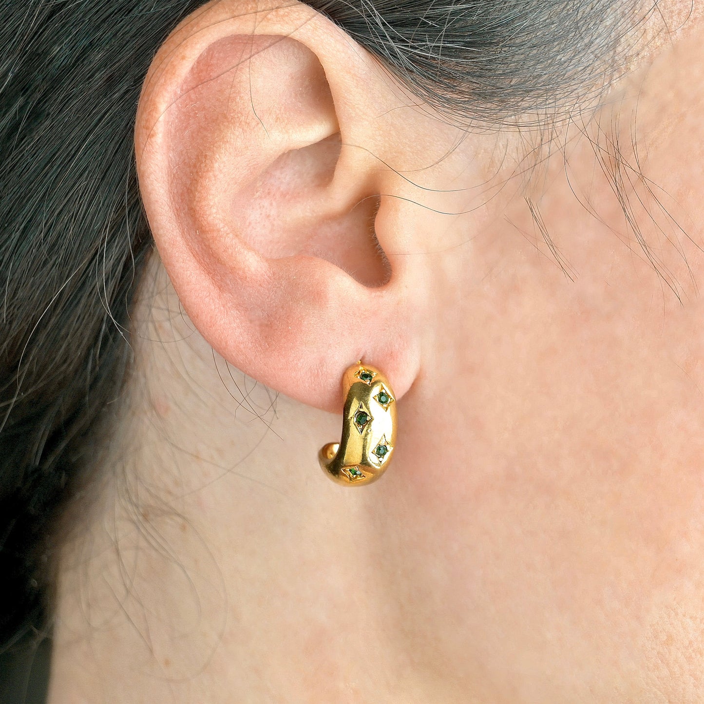 Chunky hoop earrings with green gemstones worn by a person