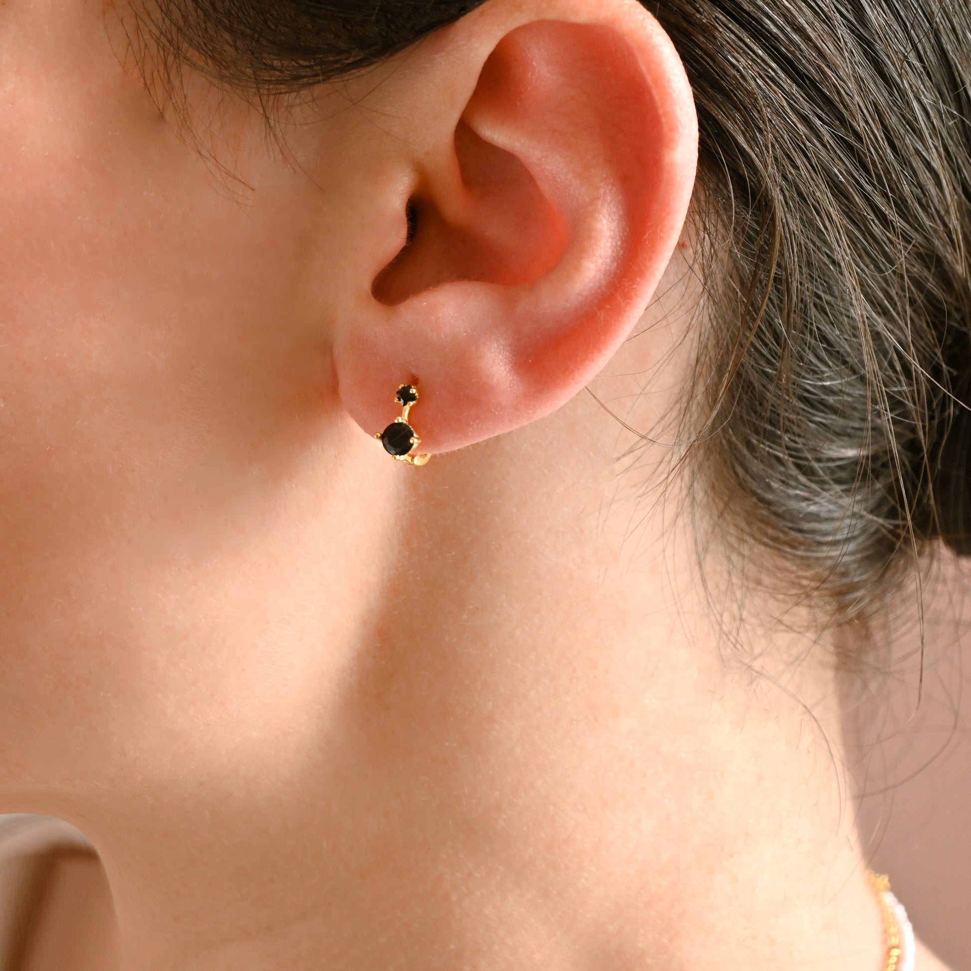 Close-up of an ear wearing a black hoop earring with gold accents.