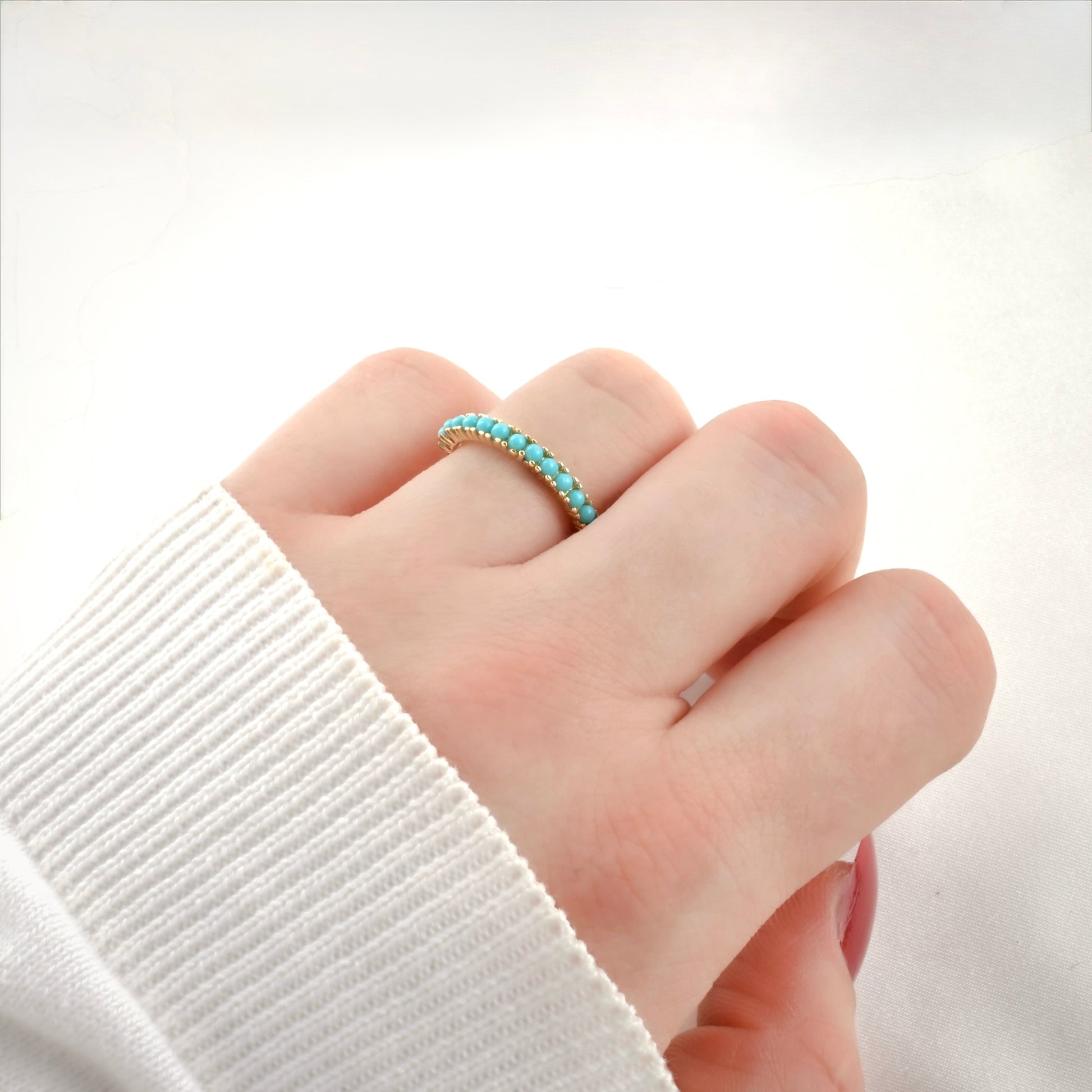 Hand wearing a turquoise beaded ring  with a fist pose on a plain background