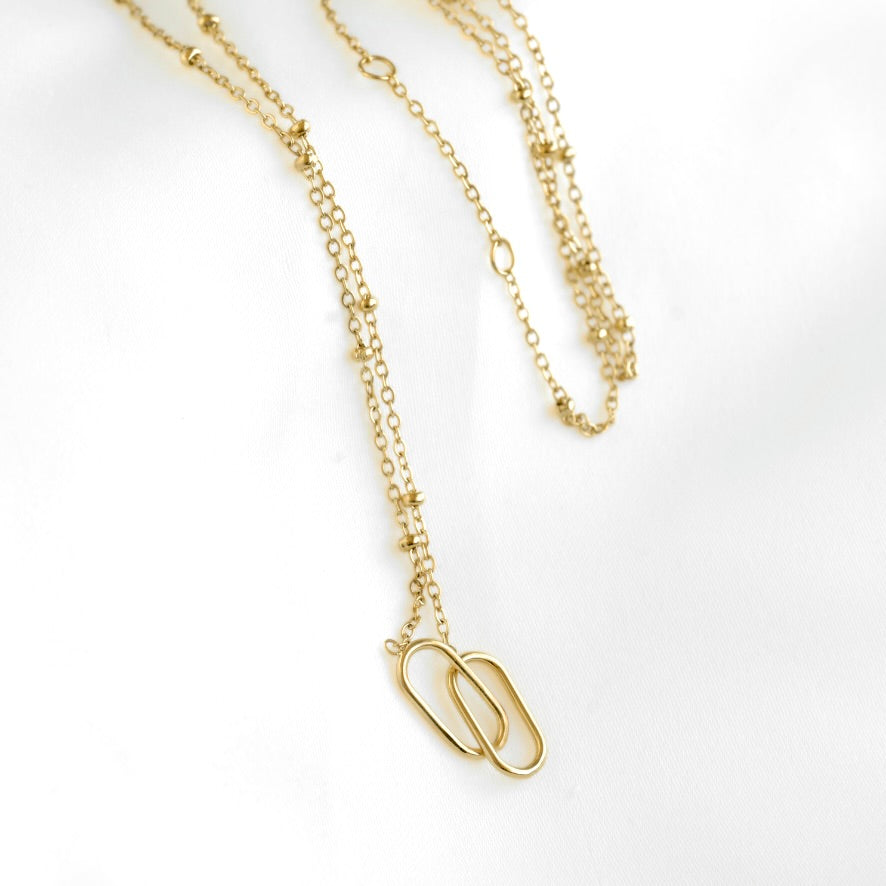 A delicate gold chain necklace featuring a double interlocking paperclip pendant, displayed on a clean white background.