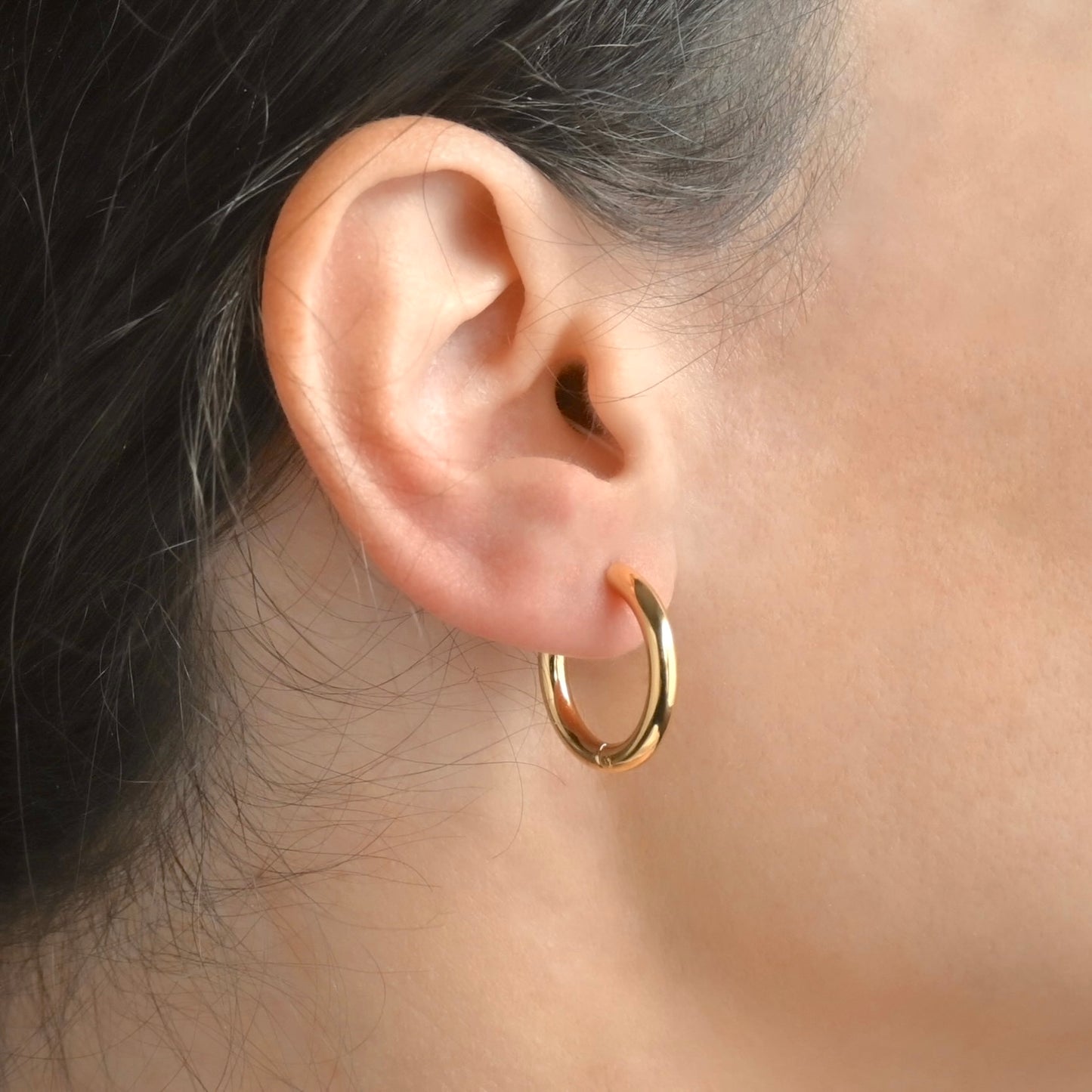 Close-up of an ear wearing a gold hoop earrings with blurred background