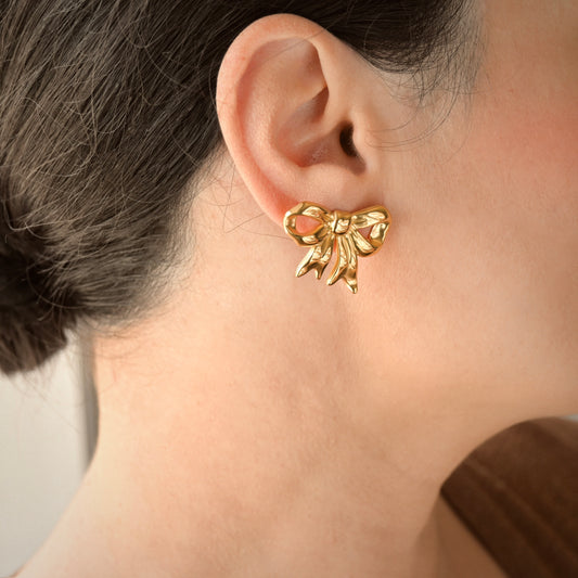 Gold bow drop earring worn by a person
