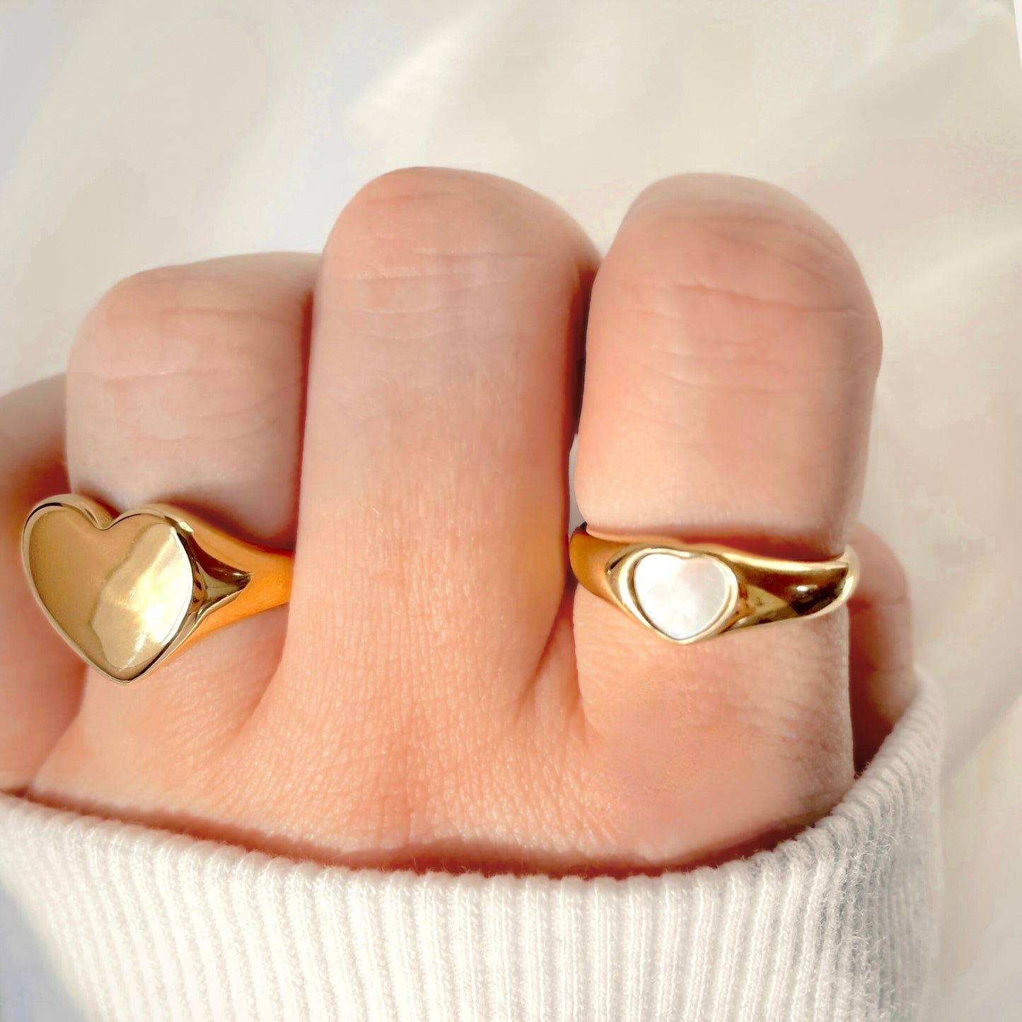Gold mother of pearl and plain oversized heart rings on a finger against a neutral background