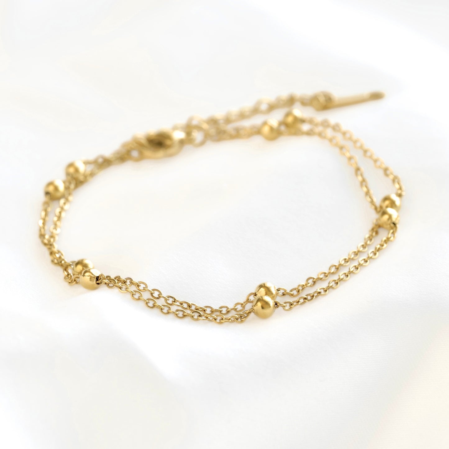 A close-up view of a delicate gold chain bracelet with small polished bead accents and an adjustable lobster clasp, displayed on a clean white background.