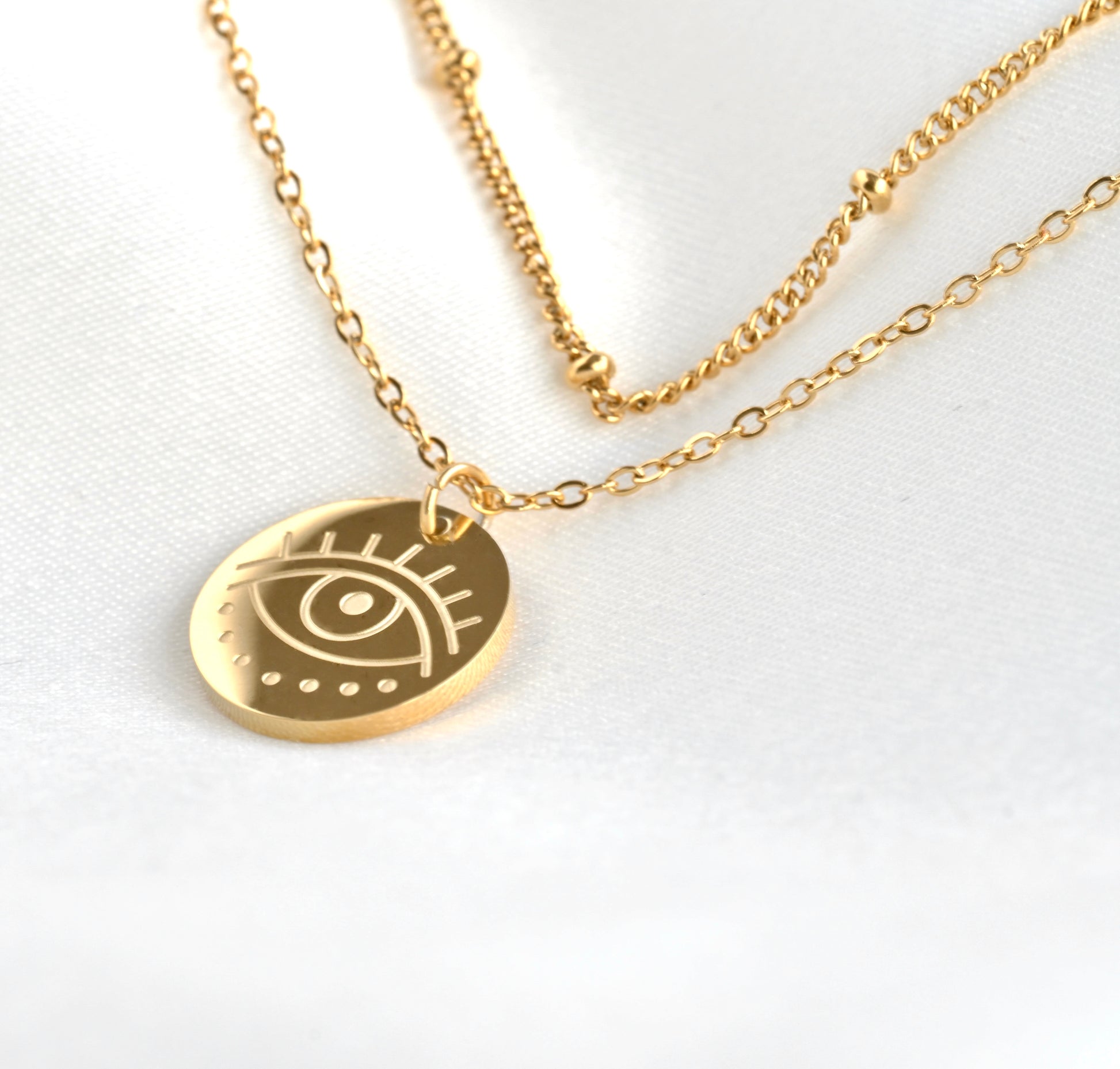 Close-up of gold necklace with a round eye engraved pendant on a white background