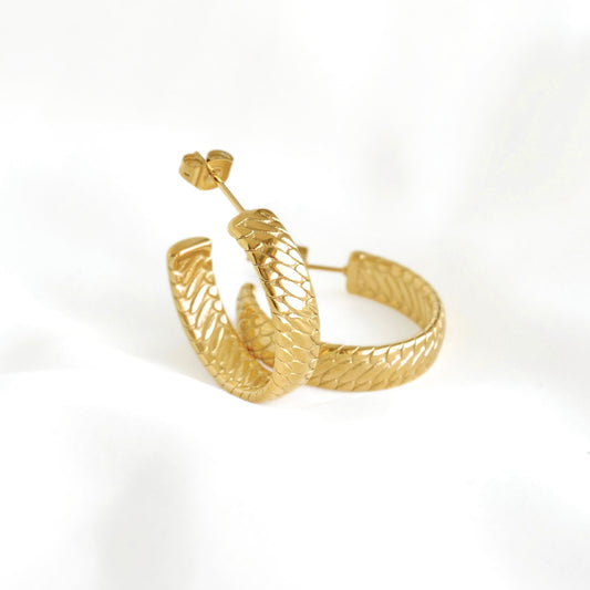 A pair of textured gold hoop earrings with a snake-like scale pattern, displayed on a clean white background.