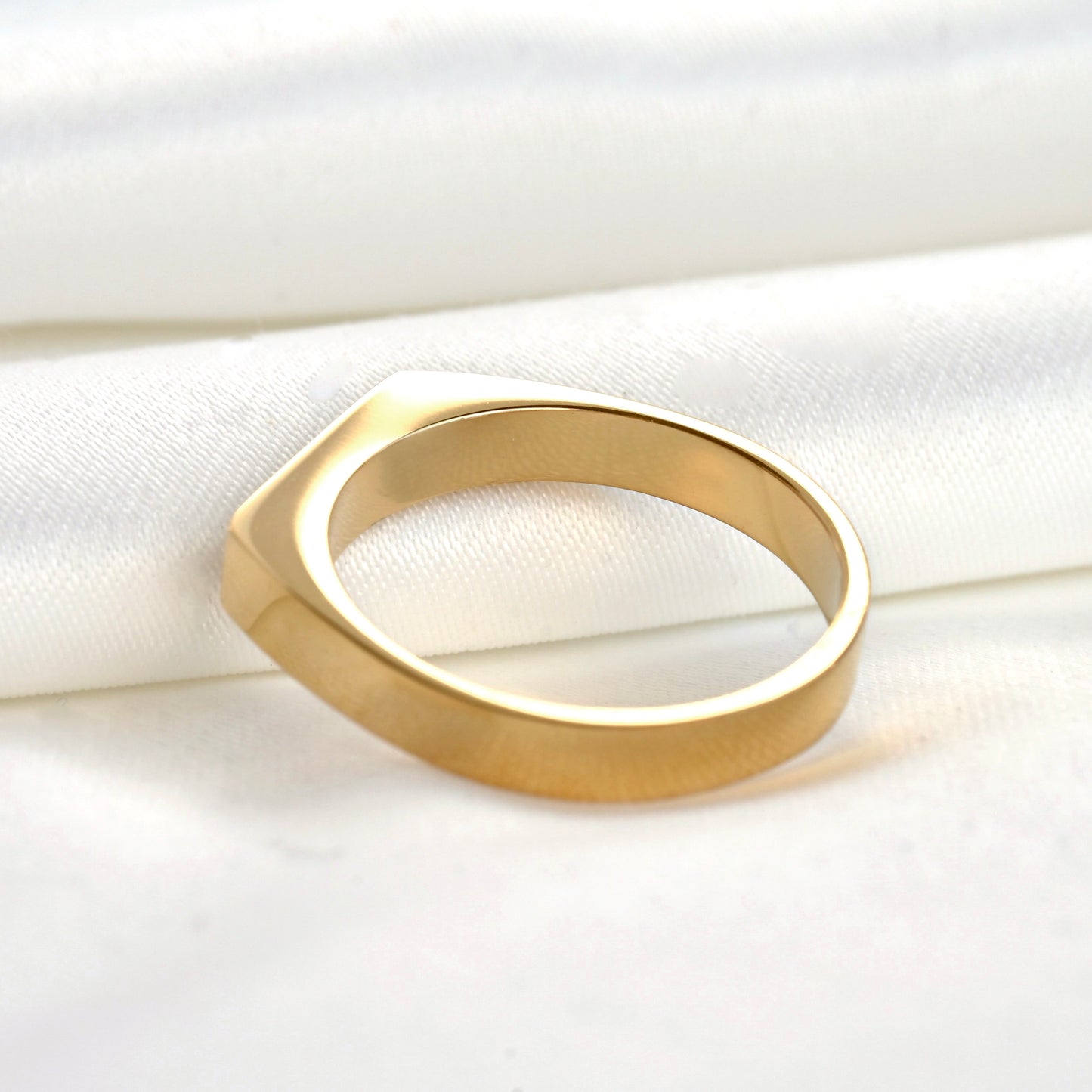 Slim gold signet ring on a white fabric background