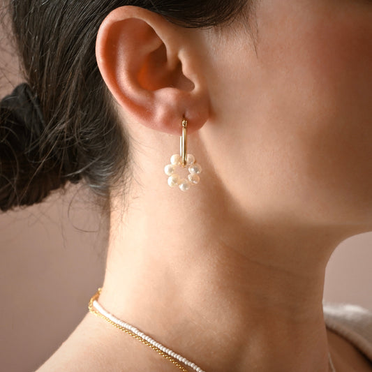 Close-up of an ear wearing a gold earring with pearls against a neutral background