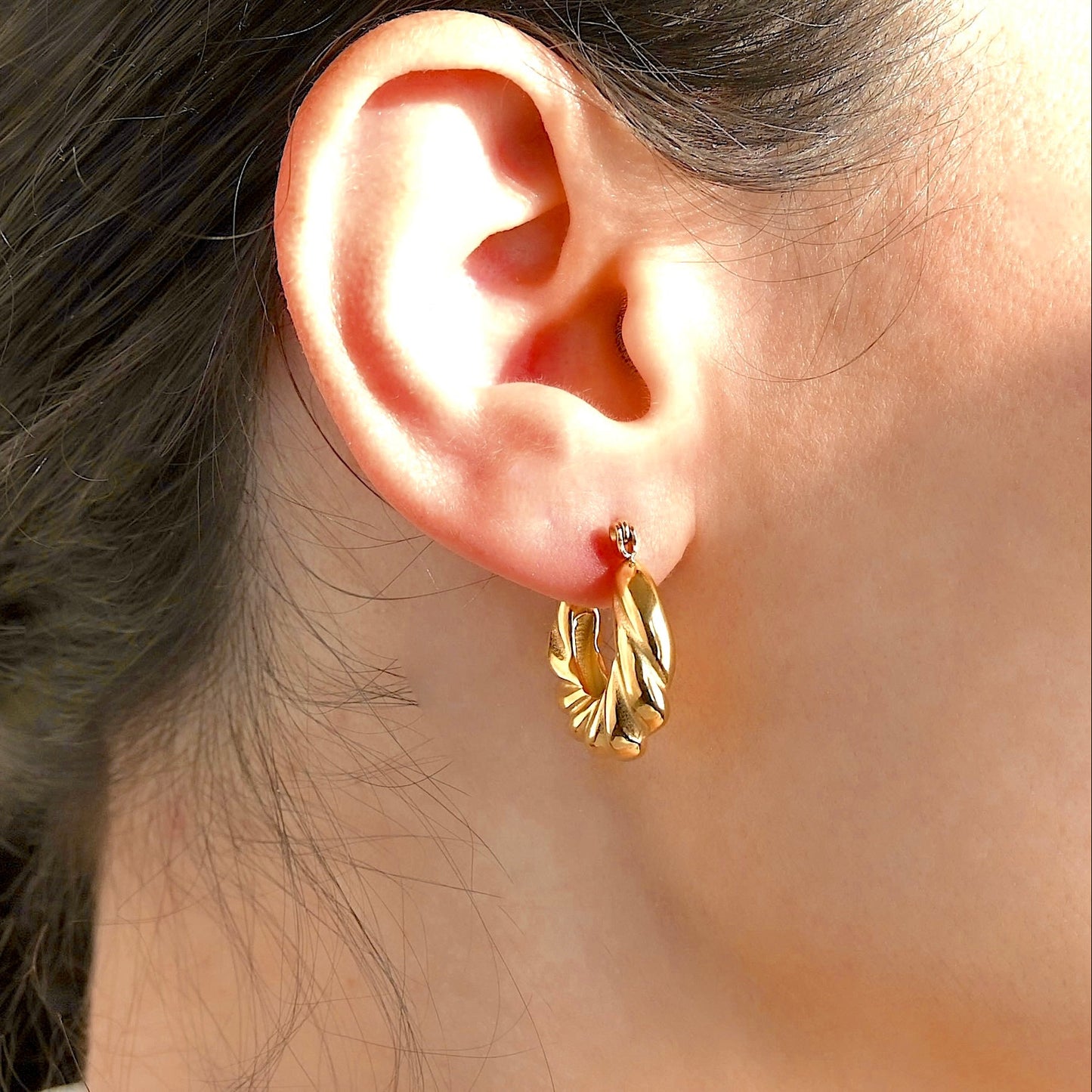 Close-up of an ear wearing twisted gold hoops with a blurred background