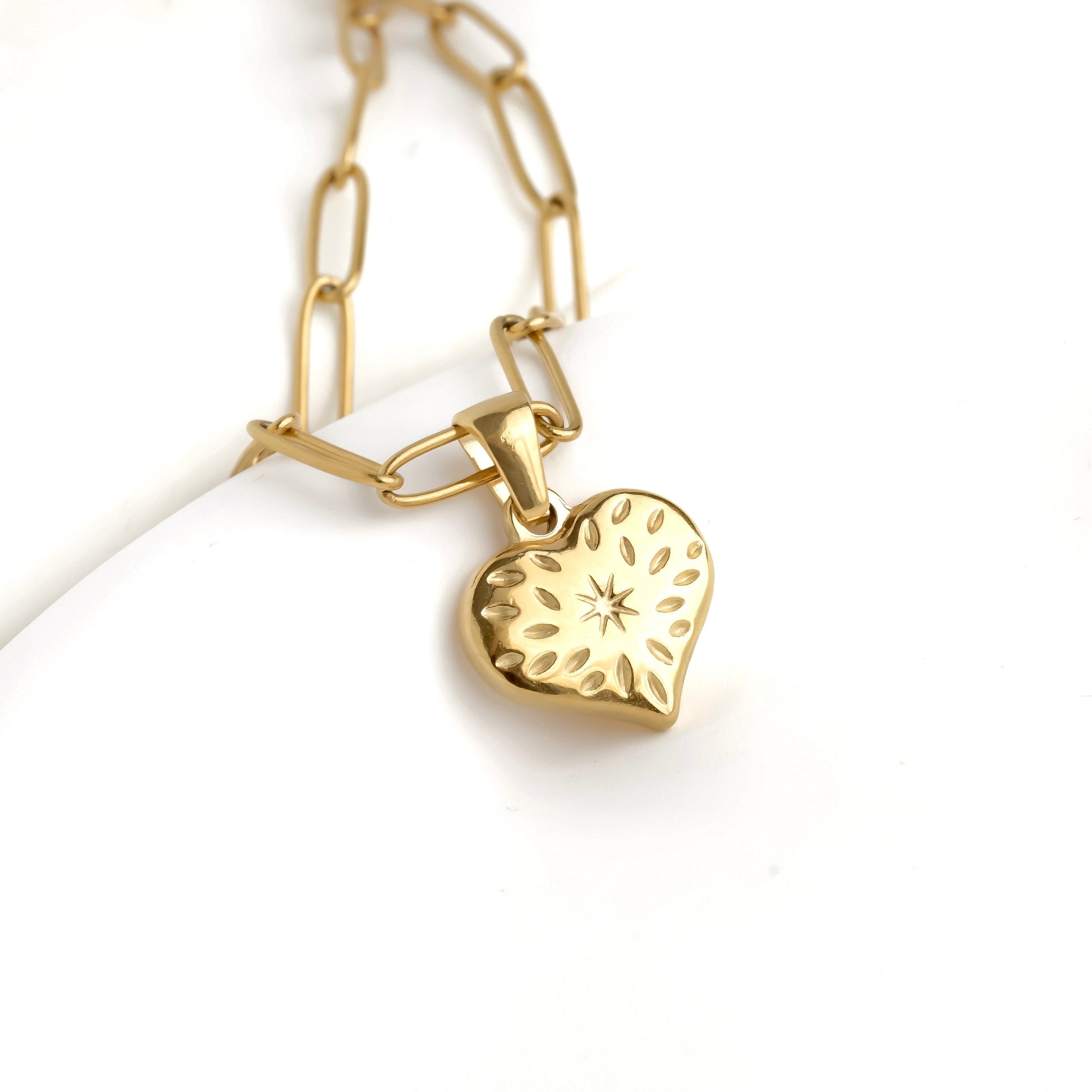 Gold paperclip heart pendant  with star design on a gold chain against a white background
