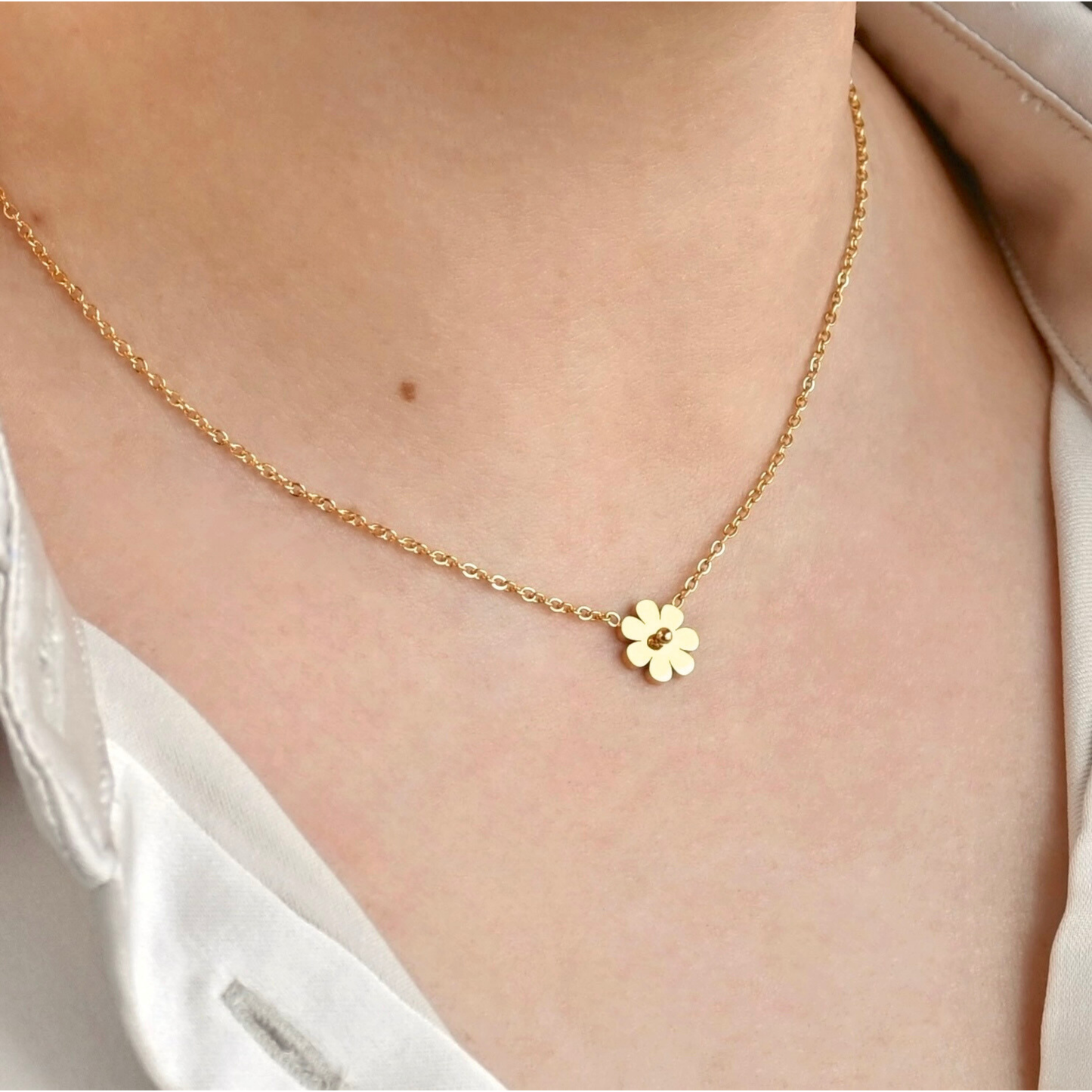 Gold necklace with a small flower pendant on a person wearing a white shirt.