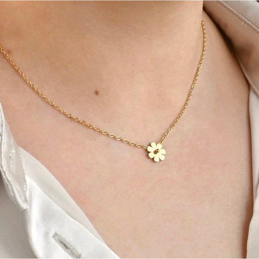 Gold necklace with a small flower pendant on a person wearing a white shirt.