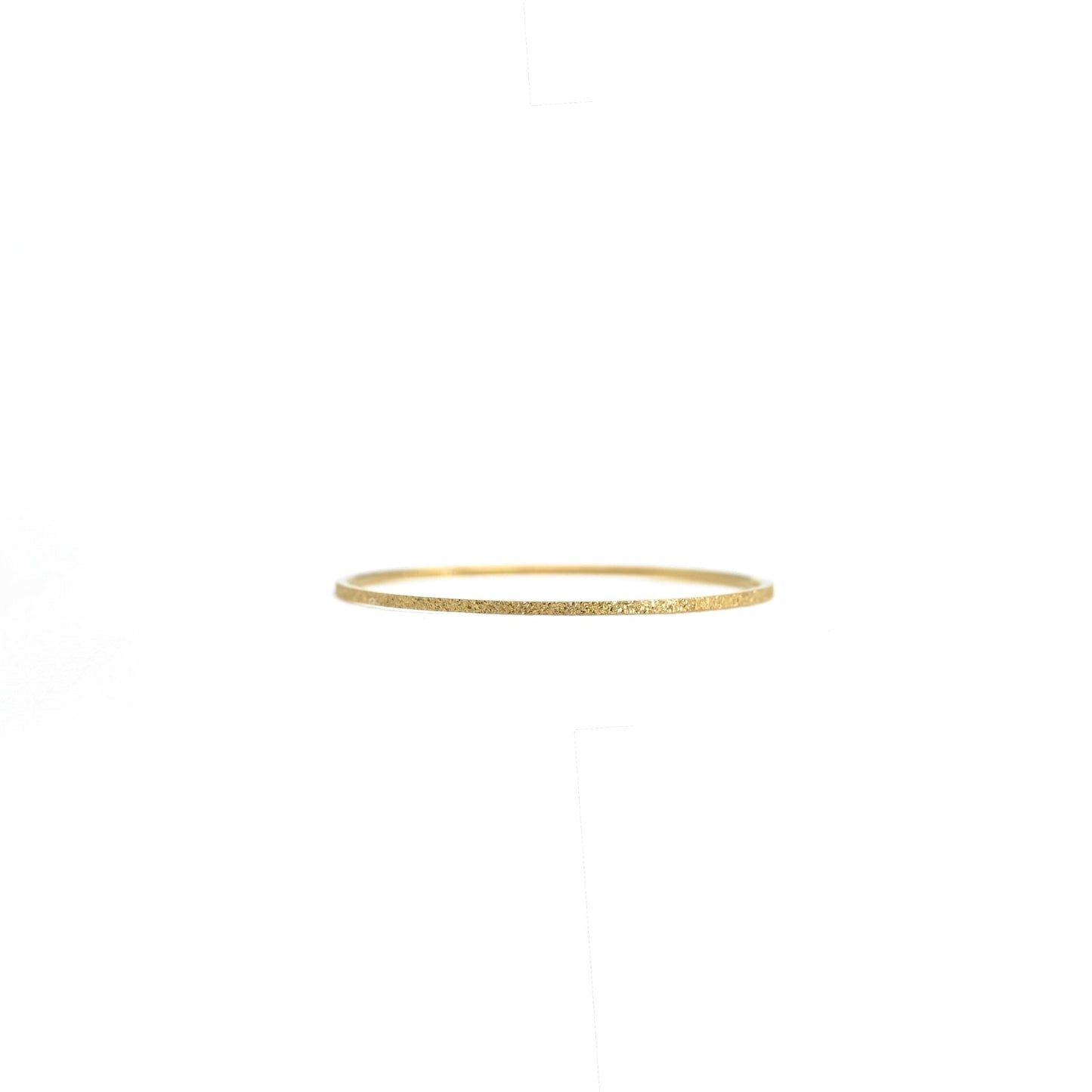 A delicate, thin gold ring with a textured, glittery finish, shown against a solid white background.