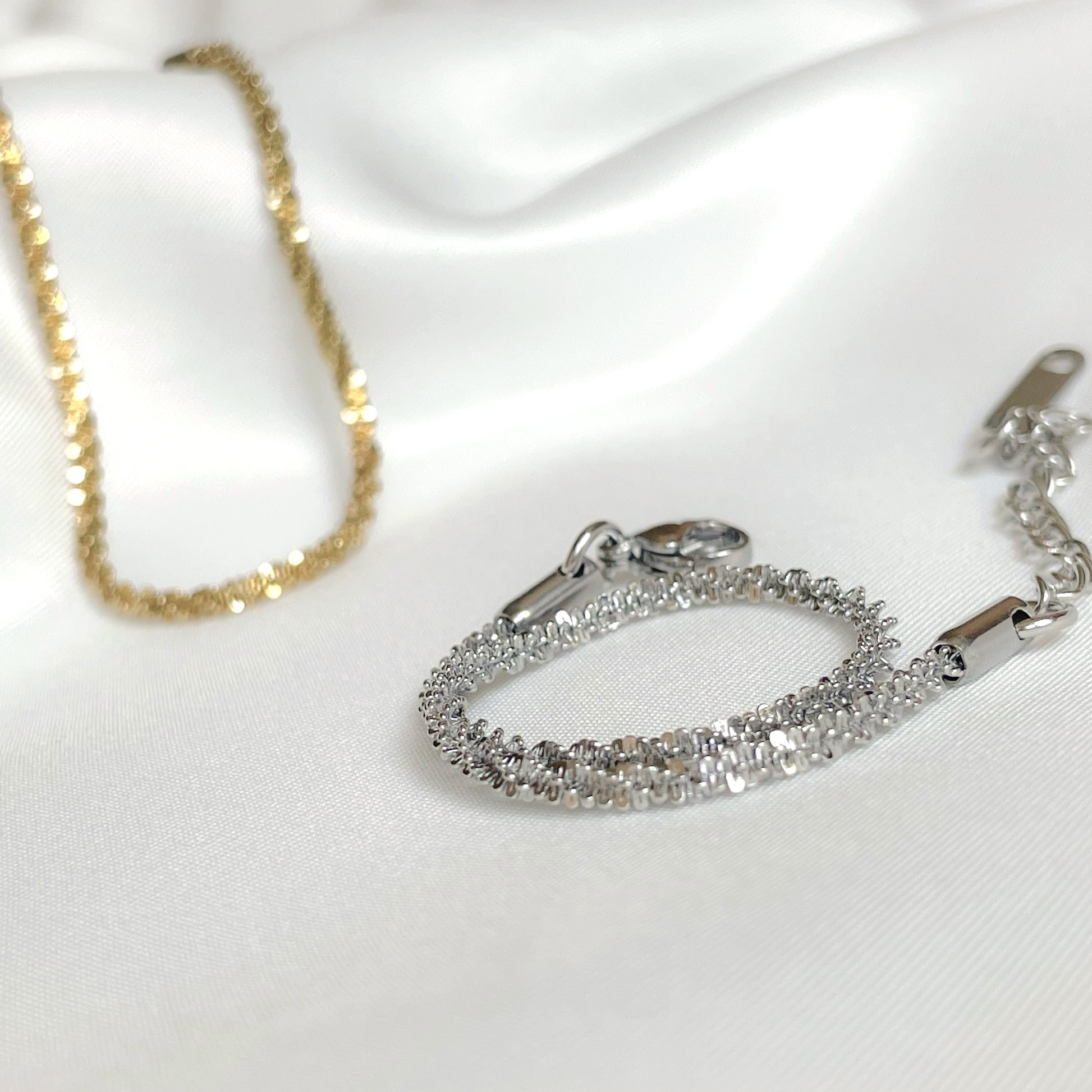 Silver rope chain bracelet with a gold chain in the background on a white satin surface