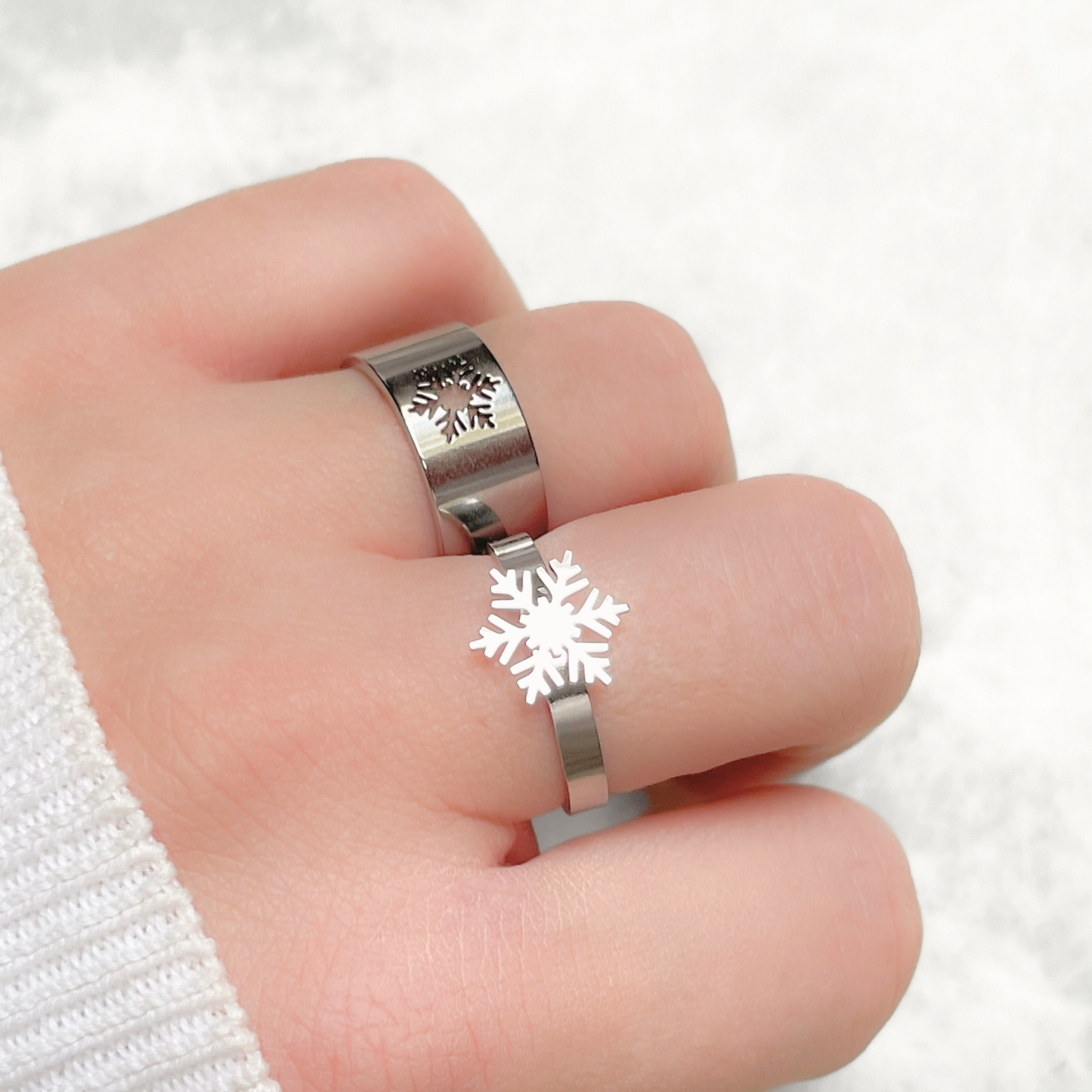 Close-up view of silver snowflake ring set on a finger against a white background