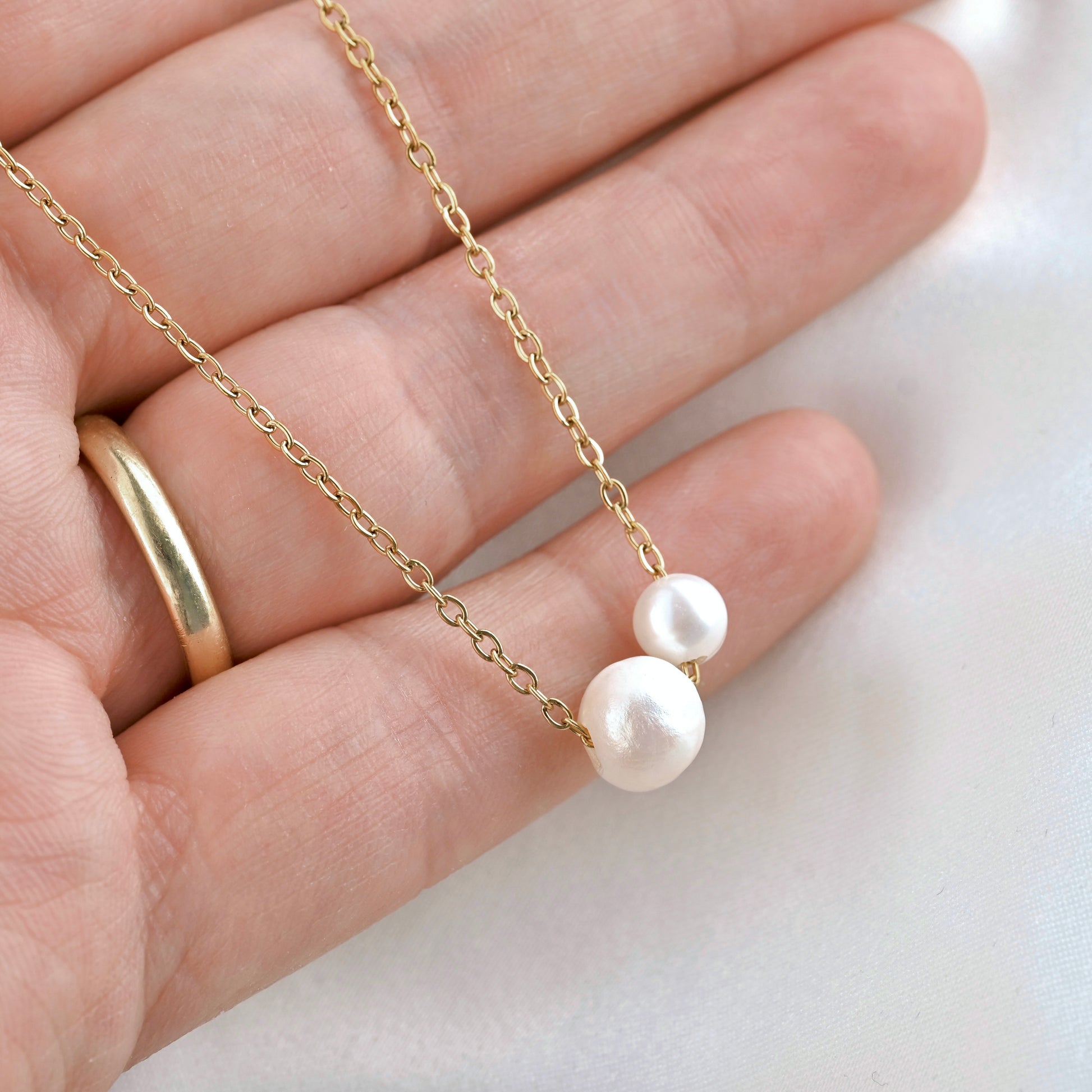 A delicate gold chain necklace with two large, irregular white baroque pearls, shown resting on a person's hand.