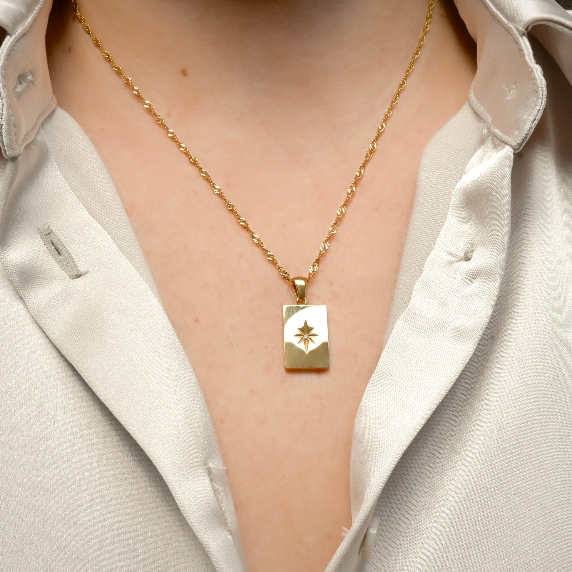 Front view of gold star necklace worn by a person in a white shirt.
